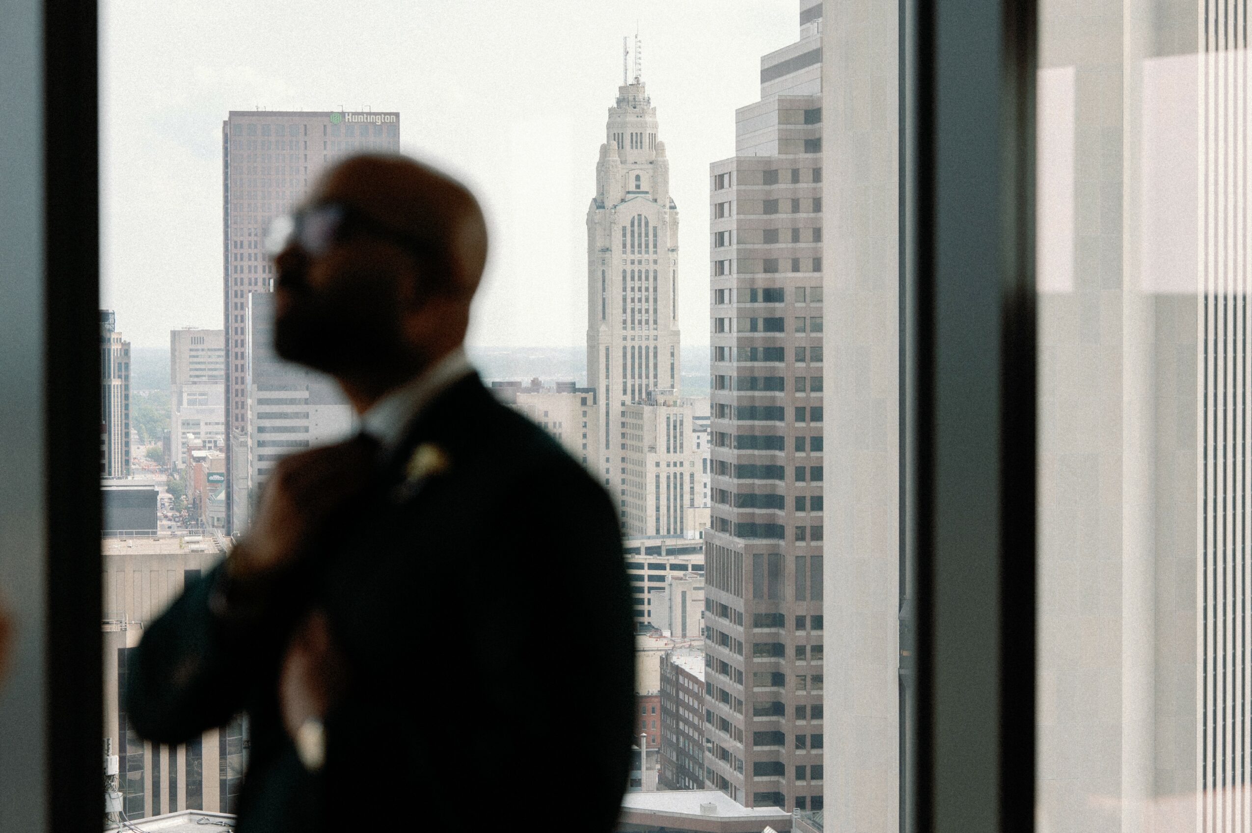 Silhouette of a person adjusting a suit collar in front of a city skyline with tall buildings, including a clock tower.