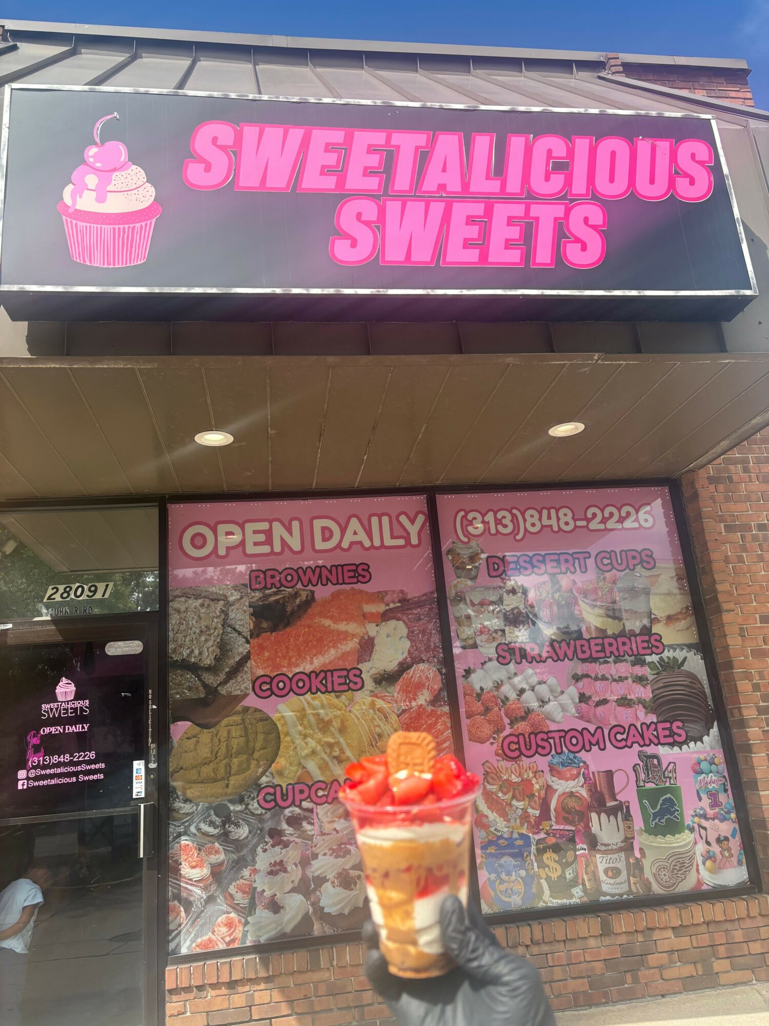 Storefront with pink sign reading 'SWEET & SUSPICIOUS SWEETS' and colorful window displays, including a drink with a straw.
