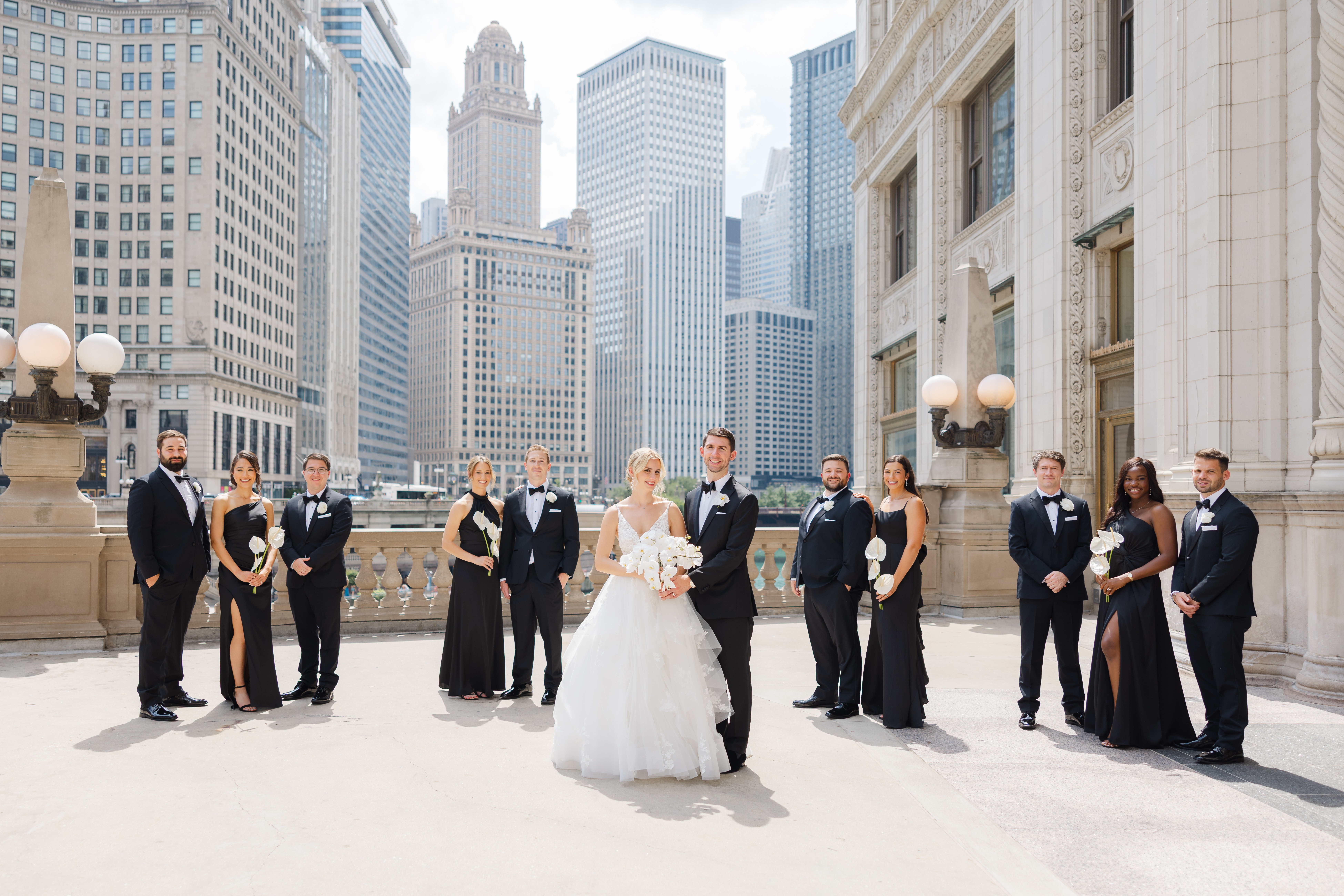 Group of people in formal attire standing outdoors on a city rooftop with tall buildings in the background.