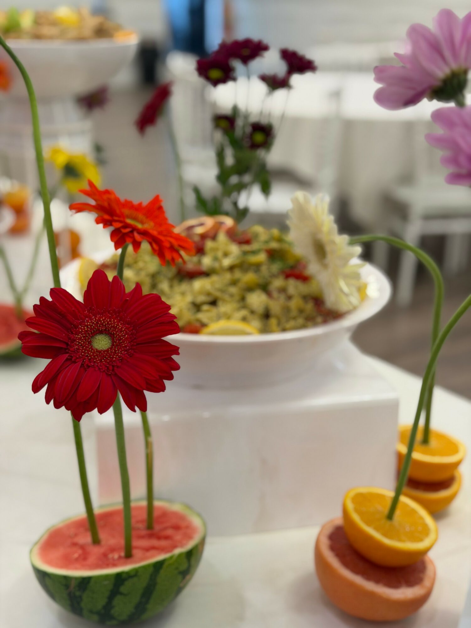 Colorful flowers in small bowls, including red, pink, white, and purple, arranged on a white surface with a blurred background.