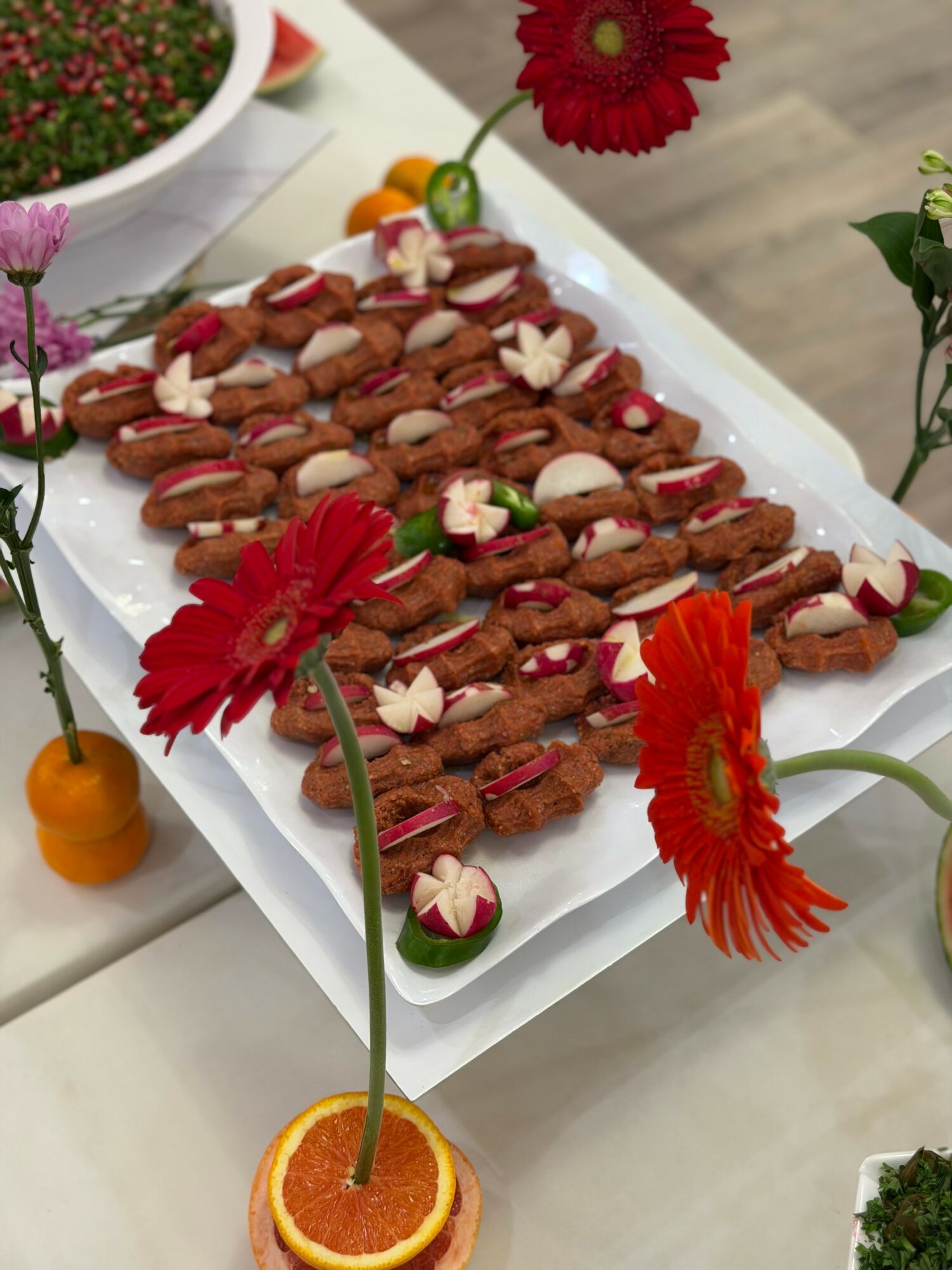 Rectangular white tray with decorated cookies, surrounded by colorful flowers and a slice of orange with a flower stem.