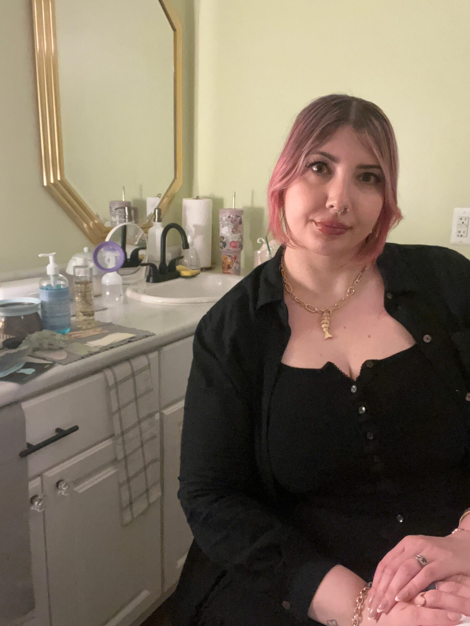 Woman with shoulder-length hair, wearing a black top, sitting at a kitchen counter with various items, smiling.