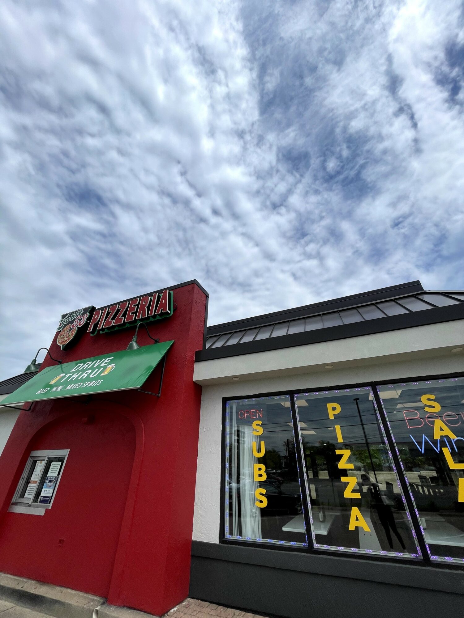 Pizza restaurant with a red exterior, large window with yellow letters, and a cloudy sky above.