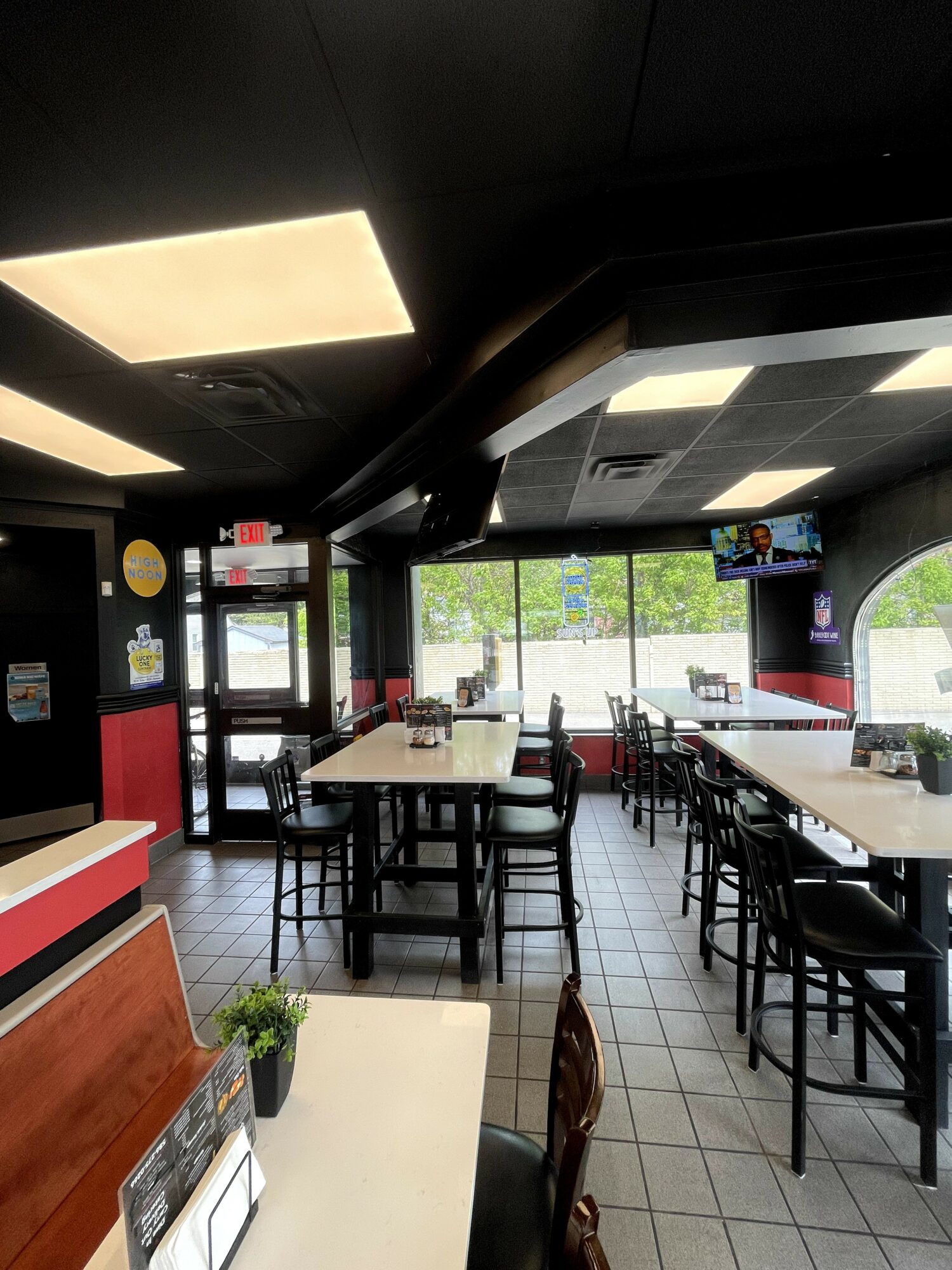 Interior of a restaurant with tables, chairs, and a door with windows, bright lighting, and a view outside.