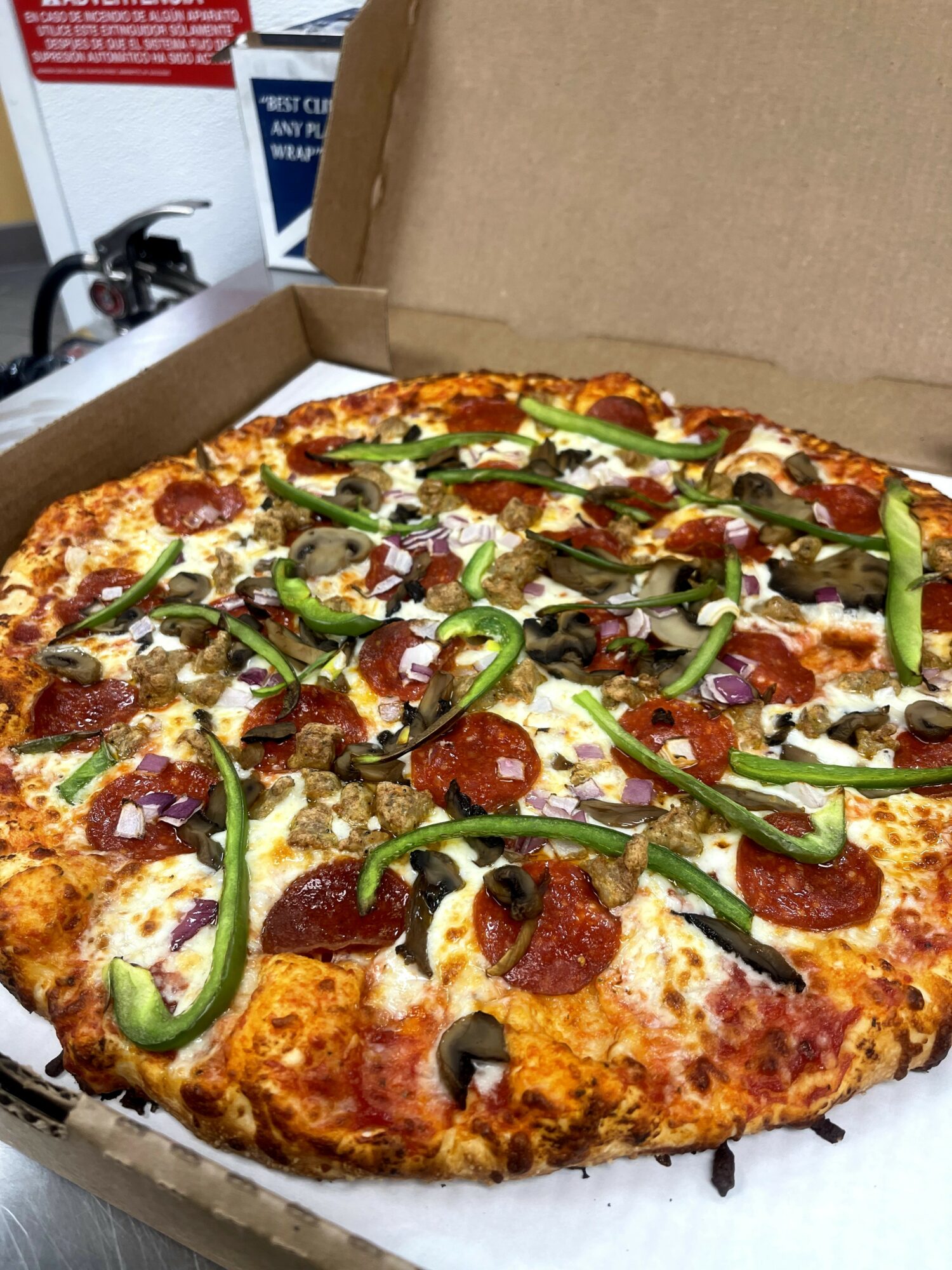 Pizza with pepperoni, green peppers, black olives, and cheese in an open box.