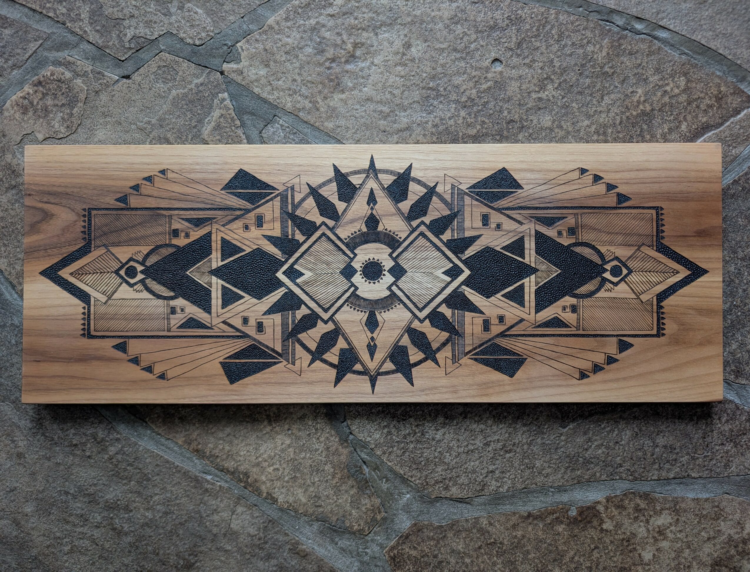 Rectangular wooden piece with geometric black and gray pattern, placed on a stone surface.