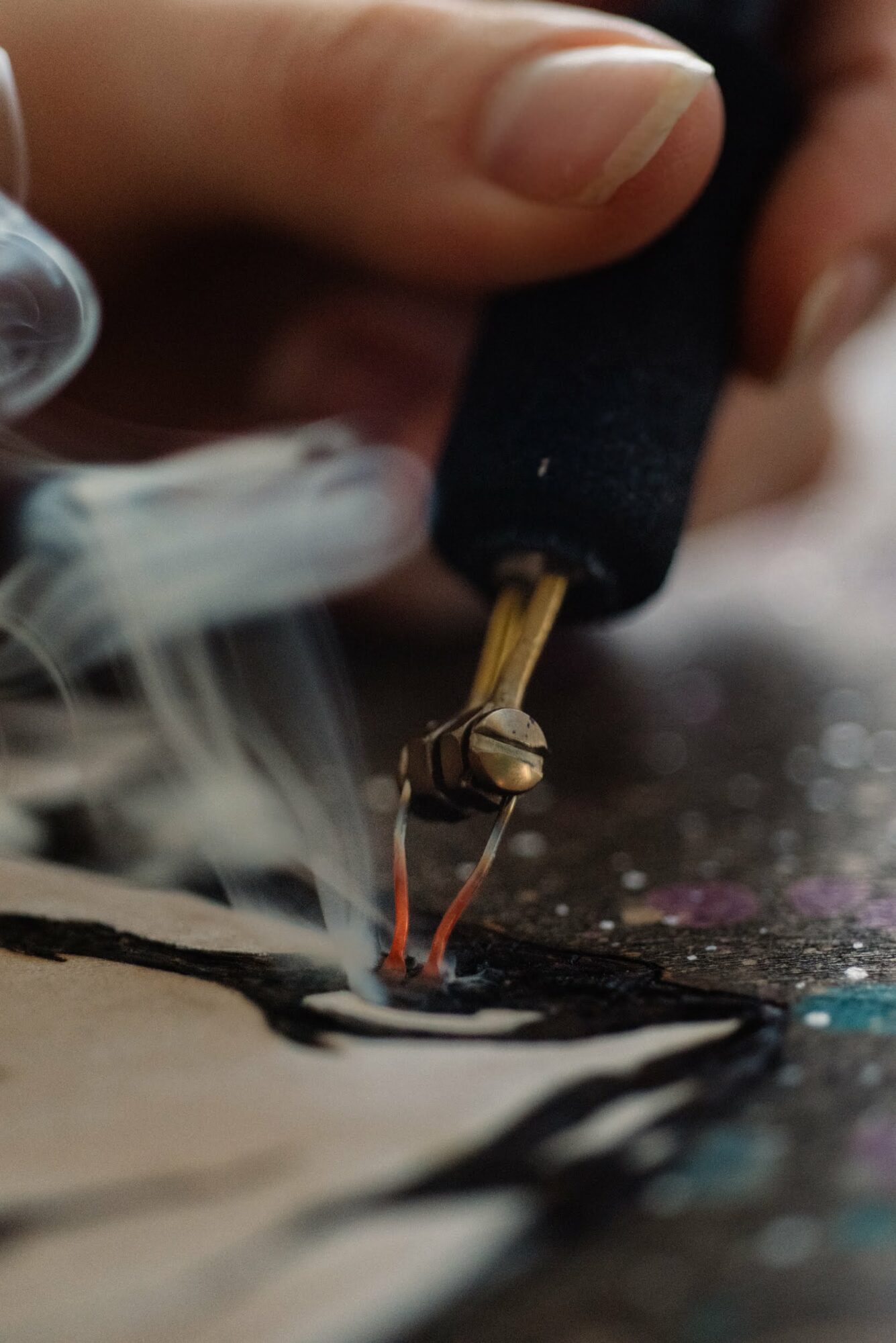 Close-up of a tattoo needle creating black ink lines on skin, with smoke or ink fumes nearby.