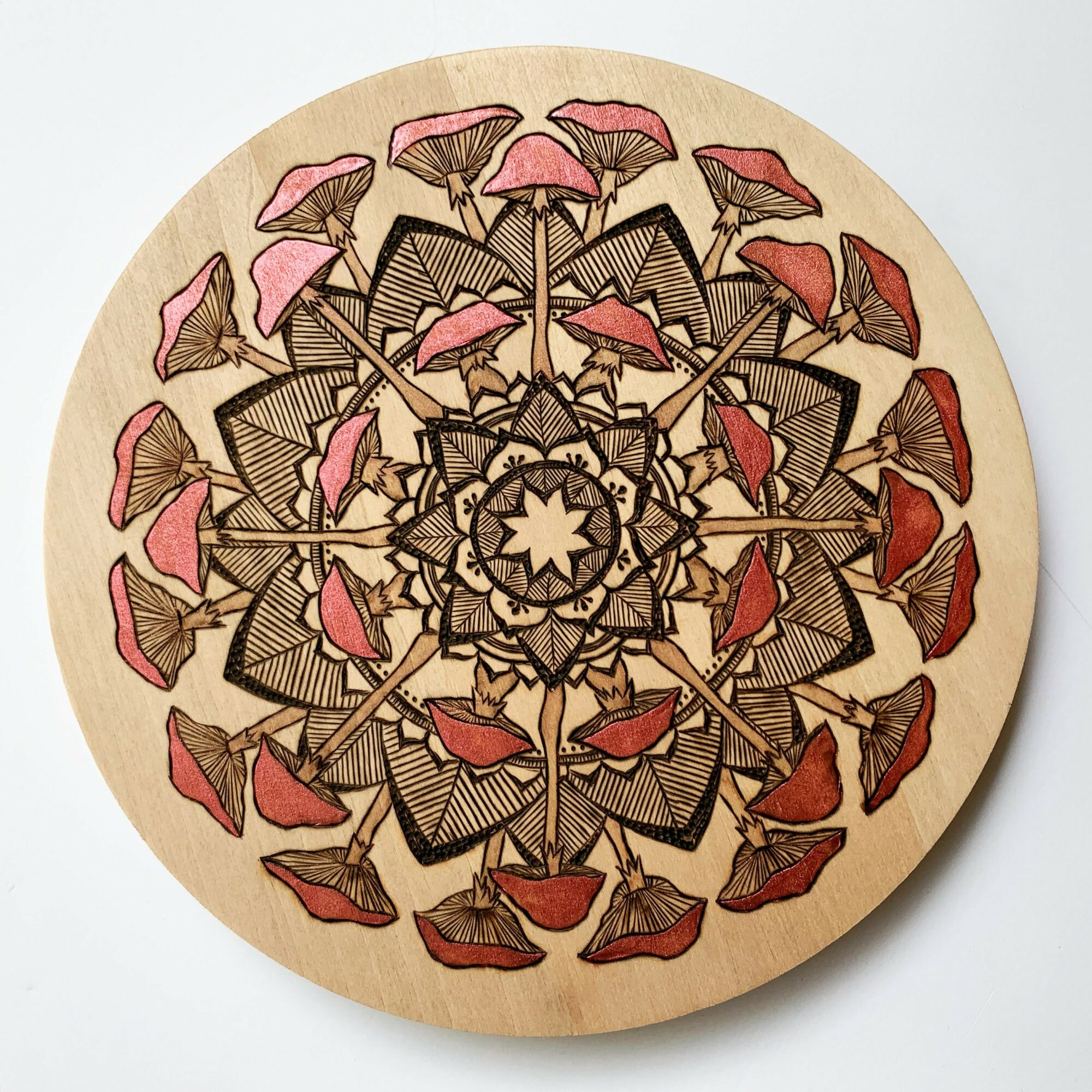 Decorative circular wooden piece with intricate black line patterns and pink and red leaf-like shapes arranged symmetrically.