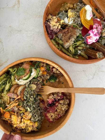 Two wooden bowls filled with colorful salads and vegetables on a white surface, with a wooden spoon in one bowl.