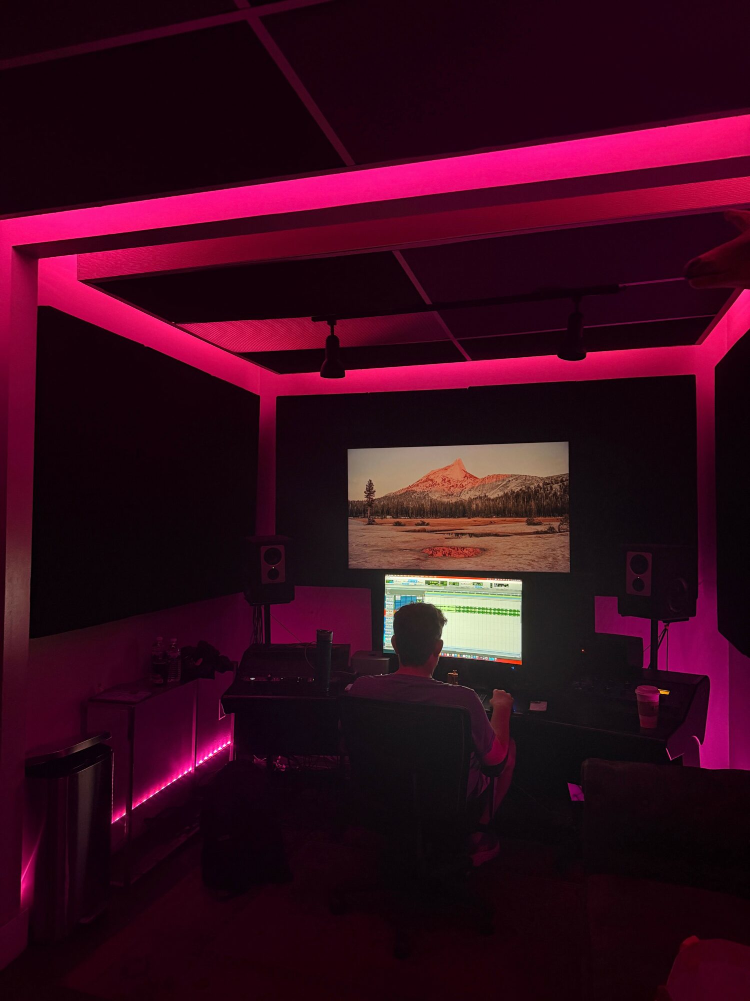 Person watching a landscape on a screen in a room with pink LED lighting, ceiling, and wall panels.