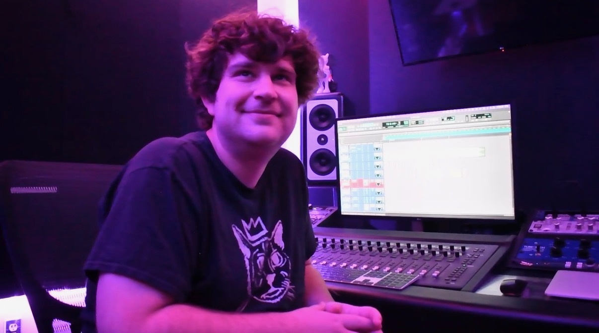 Young person with curly hair smiling in a music studio with a computer and audio equipment