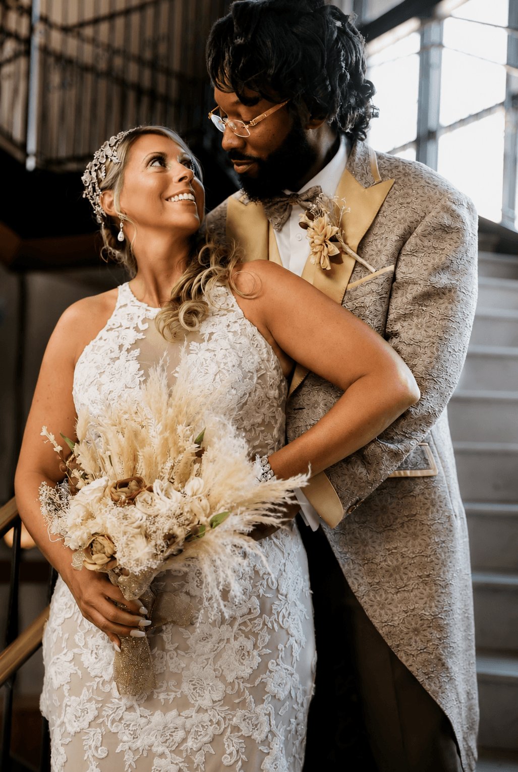 Bride and groom looking at each other indoors, bride holding a bouquet, wedding attire, warm lighting.
