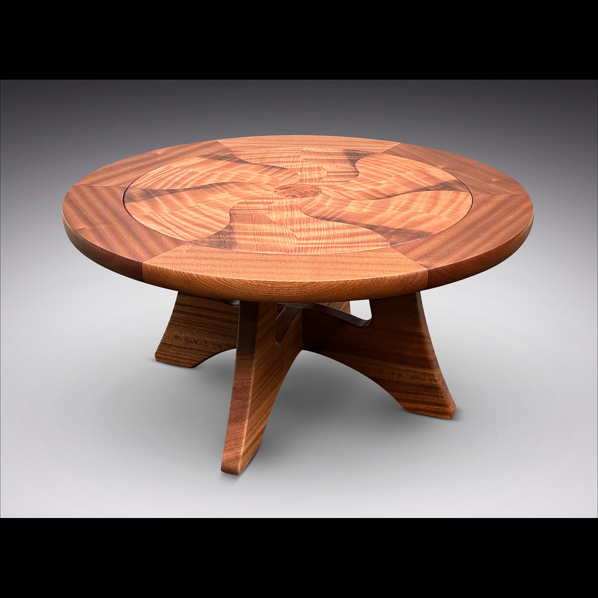 Round wooden table with a patterned top and three angled legs, against a gray background.