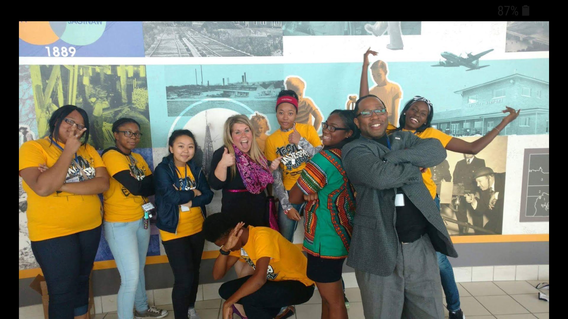 Group of people posing in front of an aviation museum display, some making gestures, some smiling, with children and adults.