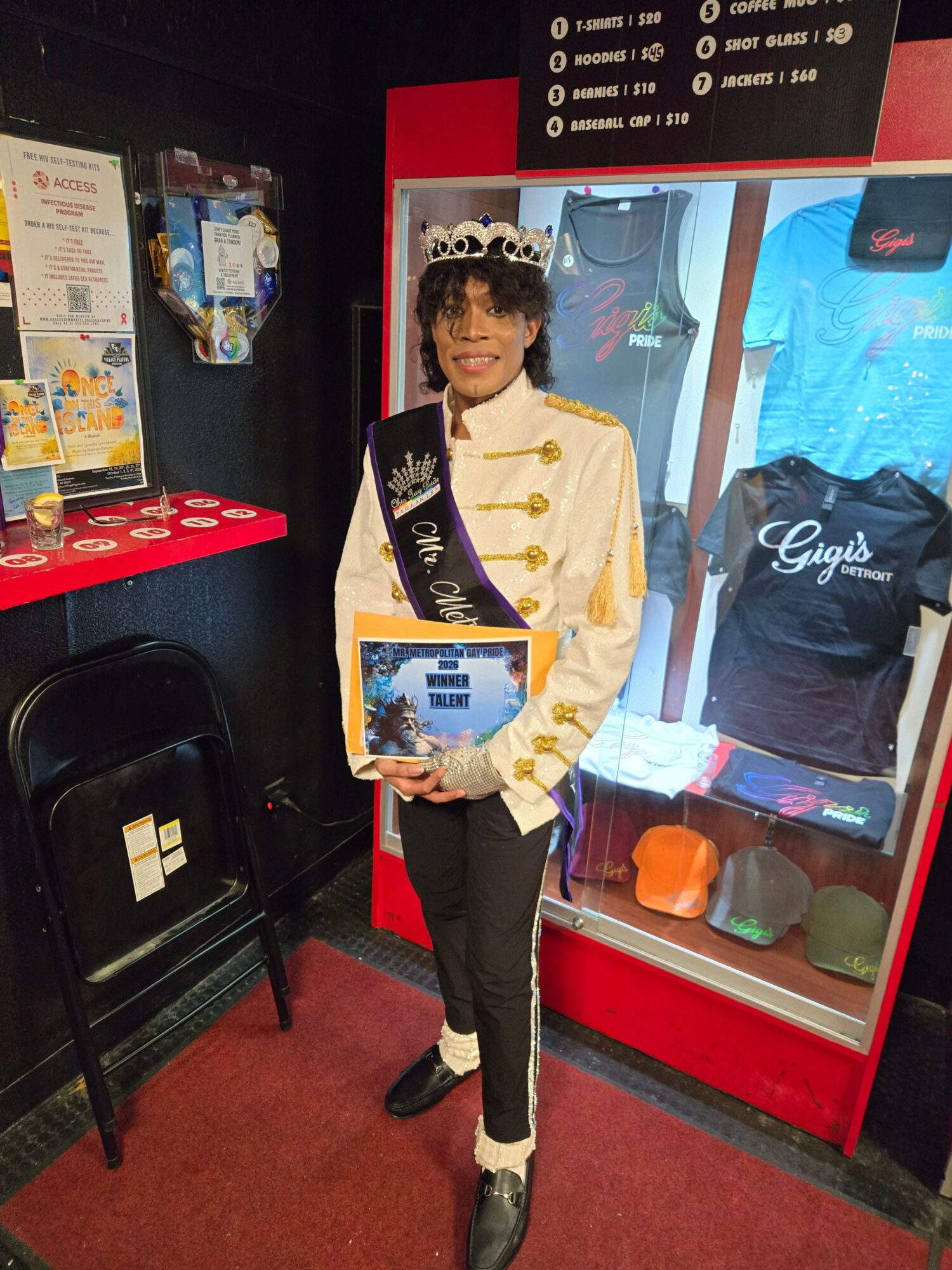 Person in a white jacket holding a framed certificate, standing inside a red display case with clothing and items behind glass.
