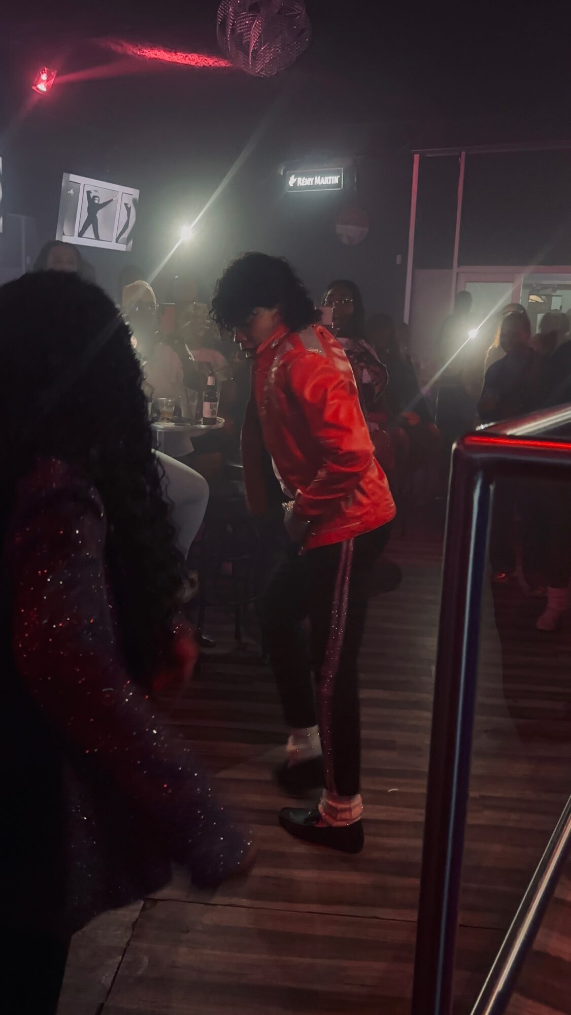 People dancing in a dimly lit nightclub with colorful lights and a disco ball overhead.