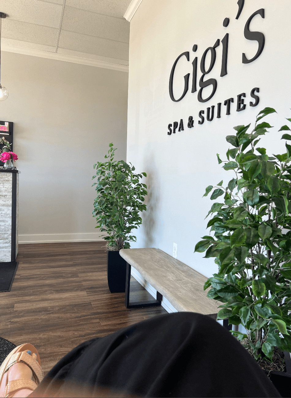 Interior of Gigi's Spa & Suites with plants, a bench, and a wall sign, viewed from a seated position.