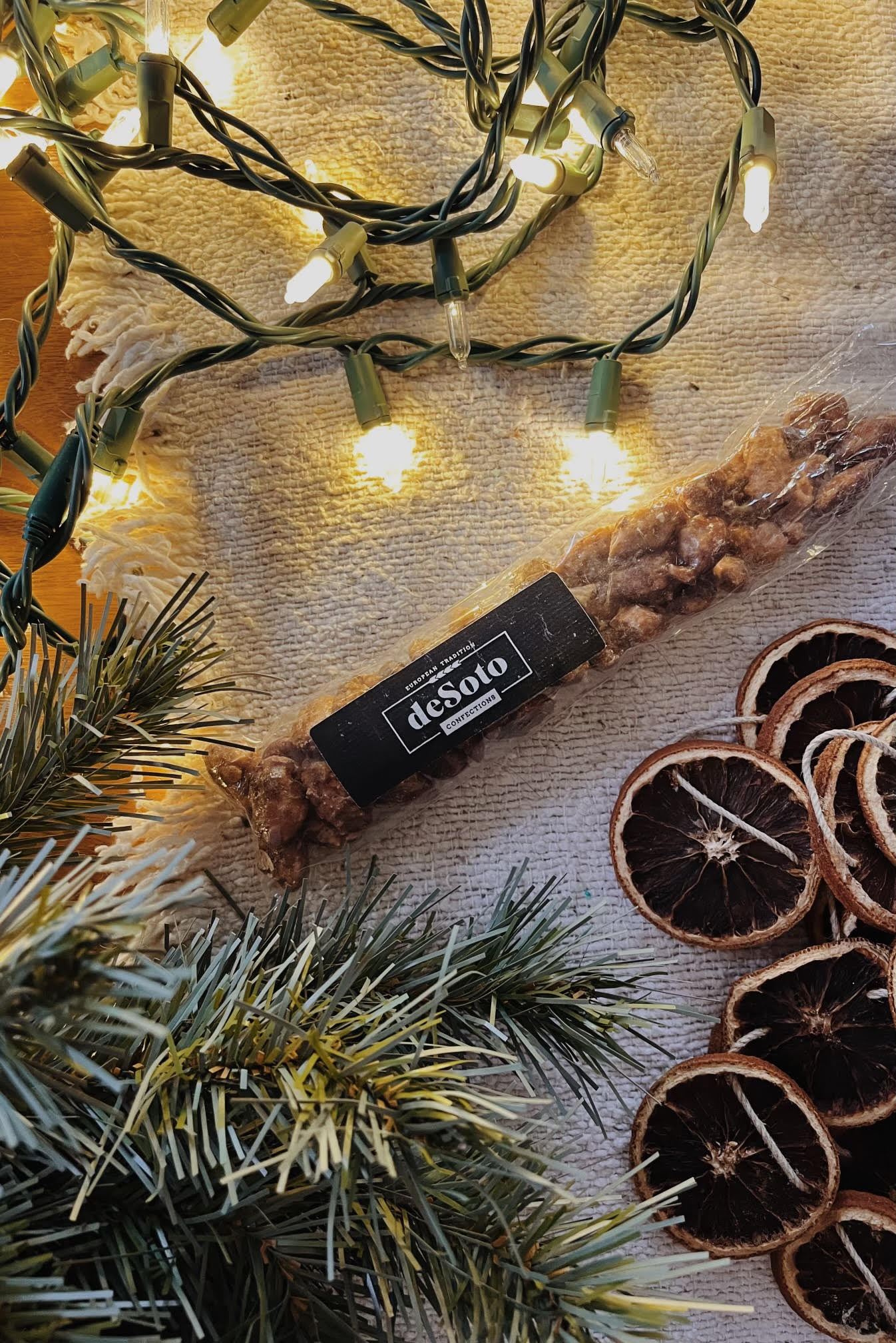 String lights, dried orange slices, and pine branches on a surface, with a black tag reading 'design' attached to a twig.