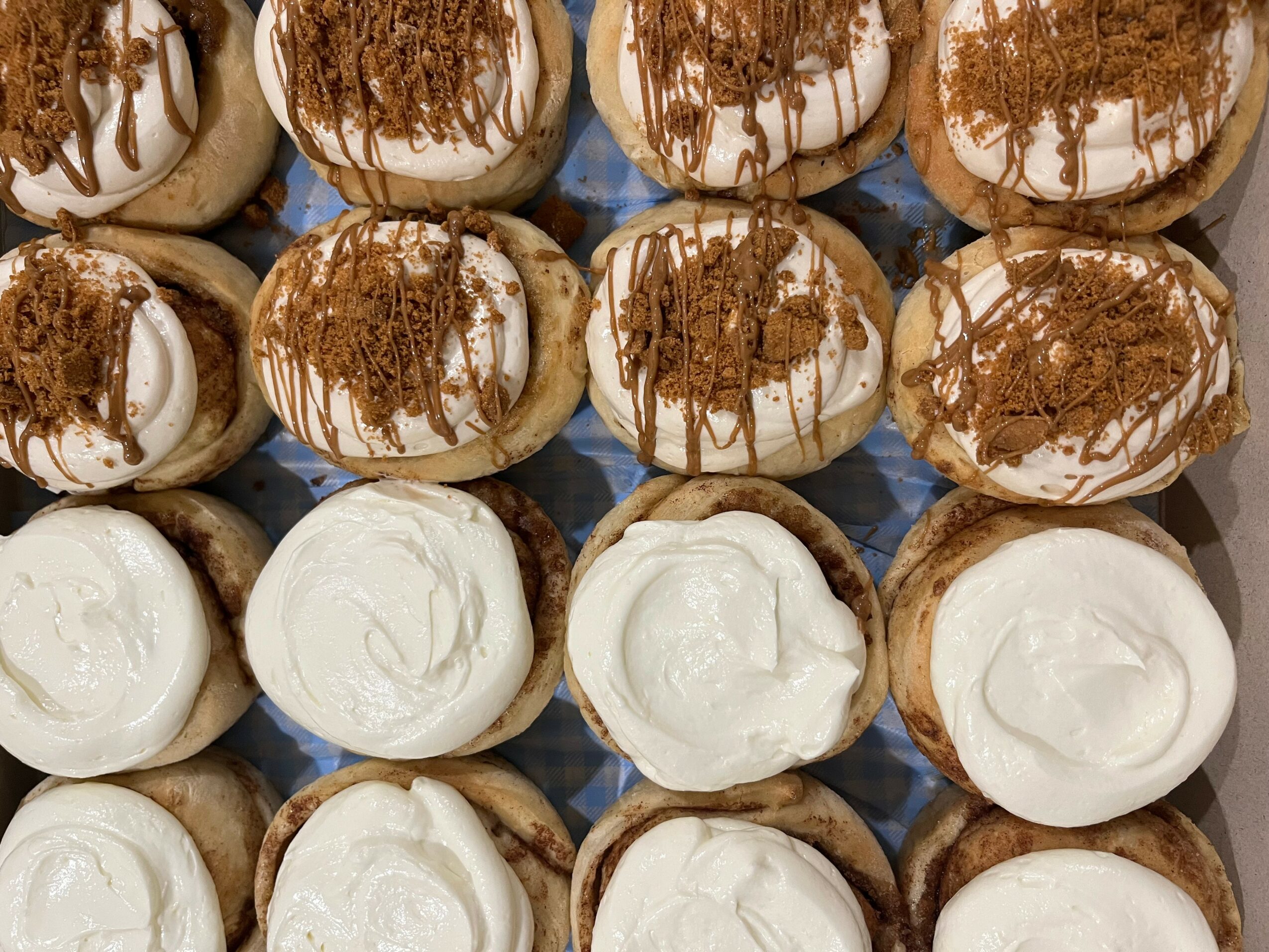 Close-up of cupcakes with white and chocolate frosting, topped with chocolate shavings, arranged in rows.