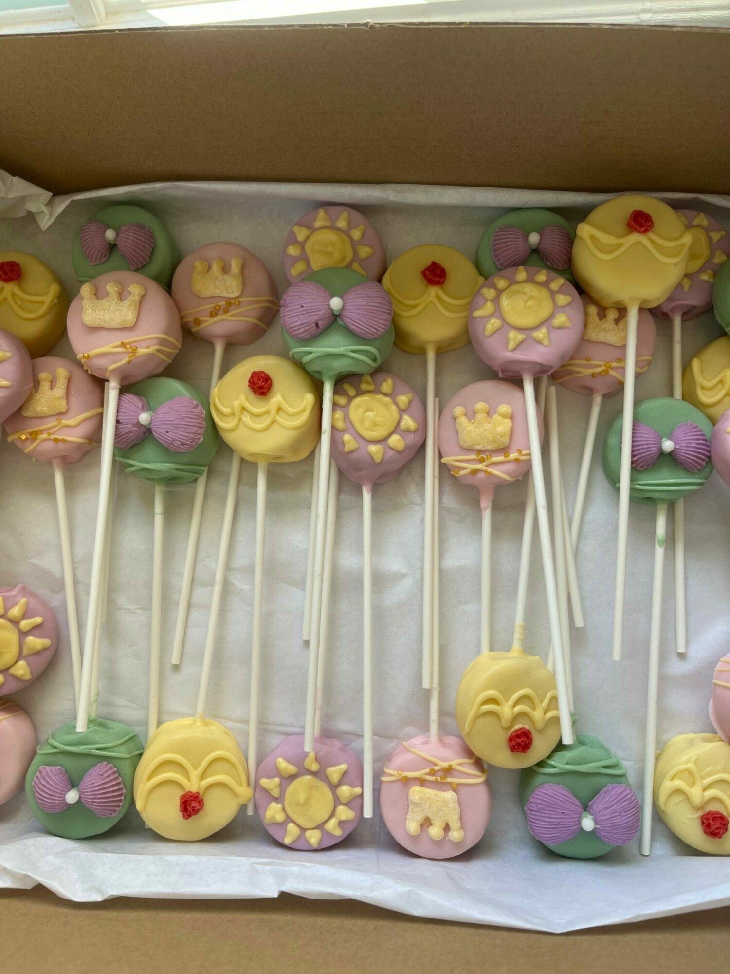 Colorful cake pops with yellow, pink, purple, and green decorations arranged in a box.