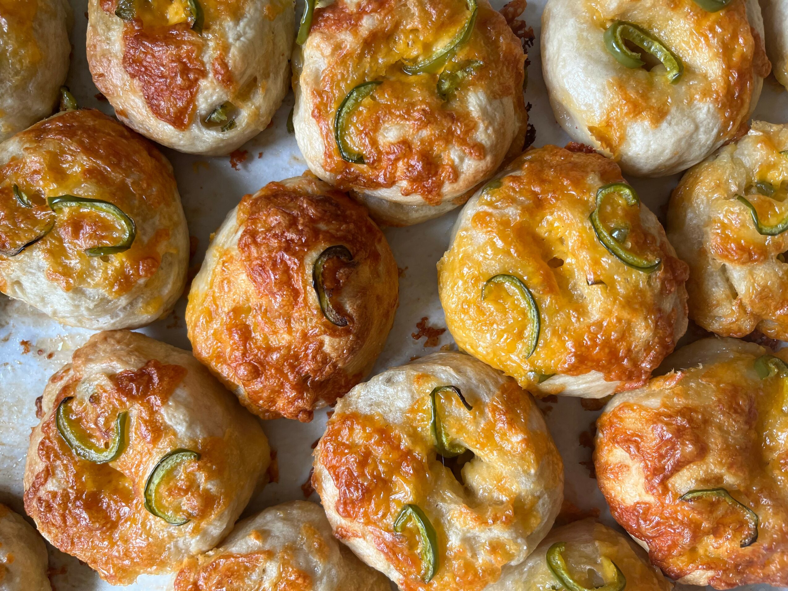 Close-up of baked cheese and jalapeño stuffed bread rolls with melted cheese and green jalapeño slices on top.