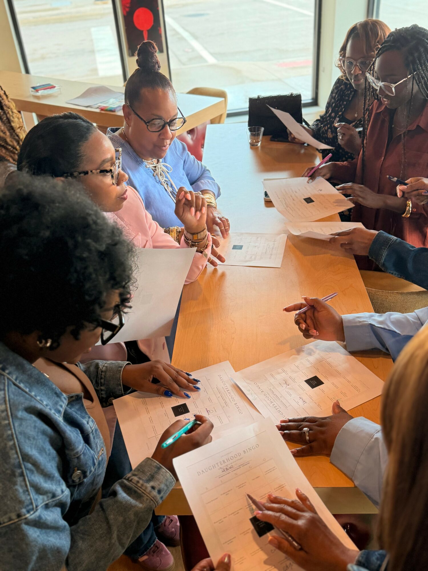 Group of diverse women sitting around a table, discussing documents and using electronic devices indoors.