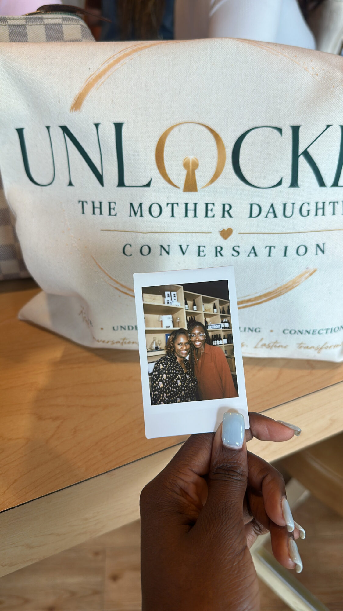 Person holding a small photo in front of a bag with the text 'UNLOCKED THE MOTHER DAUGHTER CONVERSATION'.
