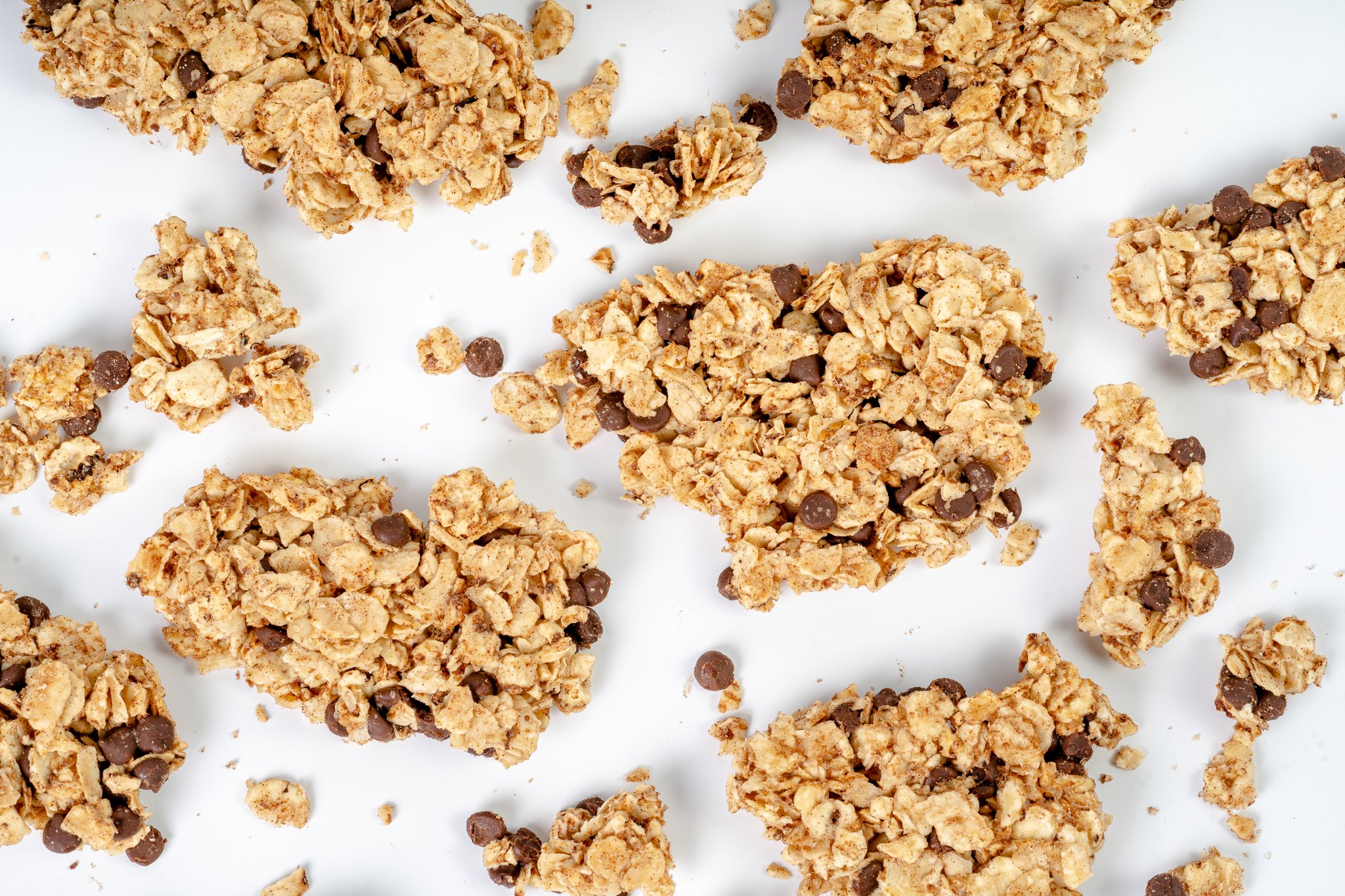 Clusters of granola scattered on a white surface, with a mix of small and large pieces.