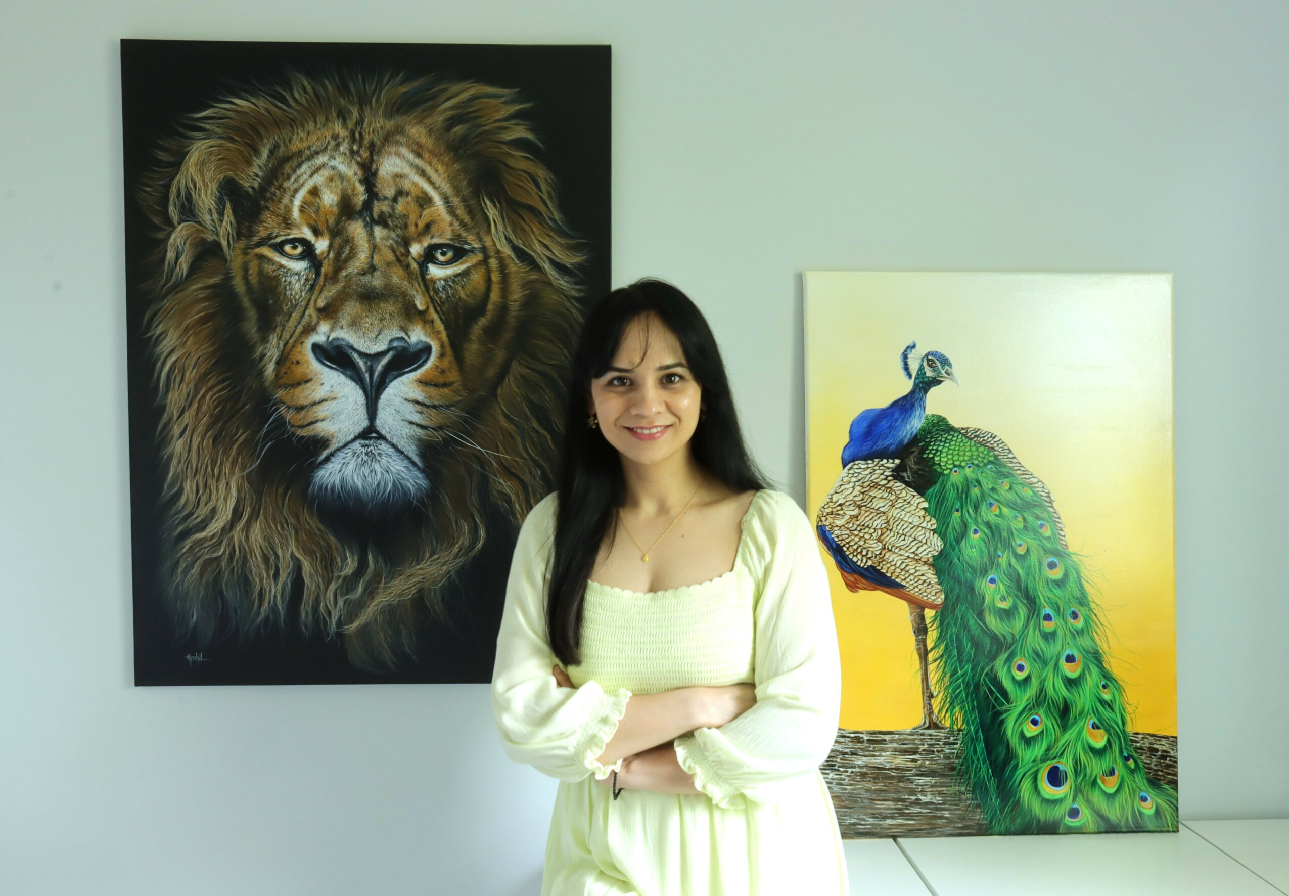 Woman standing in front of lion and peacock paintings, smiling, in an art gallery.