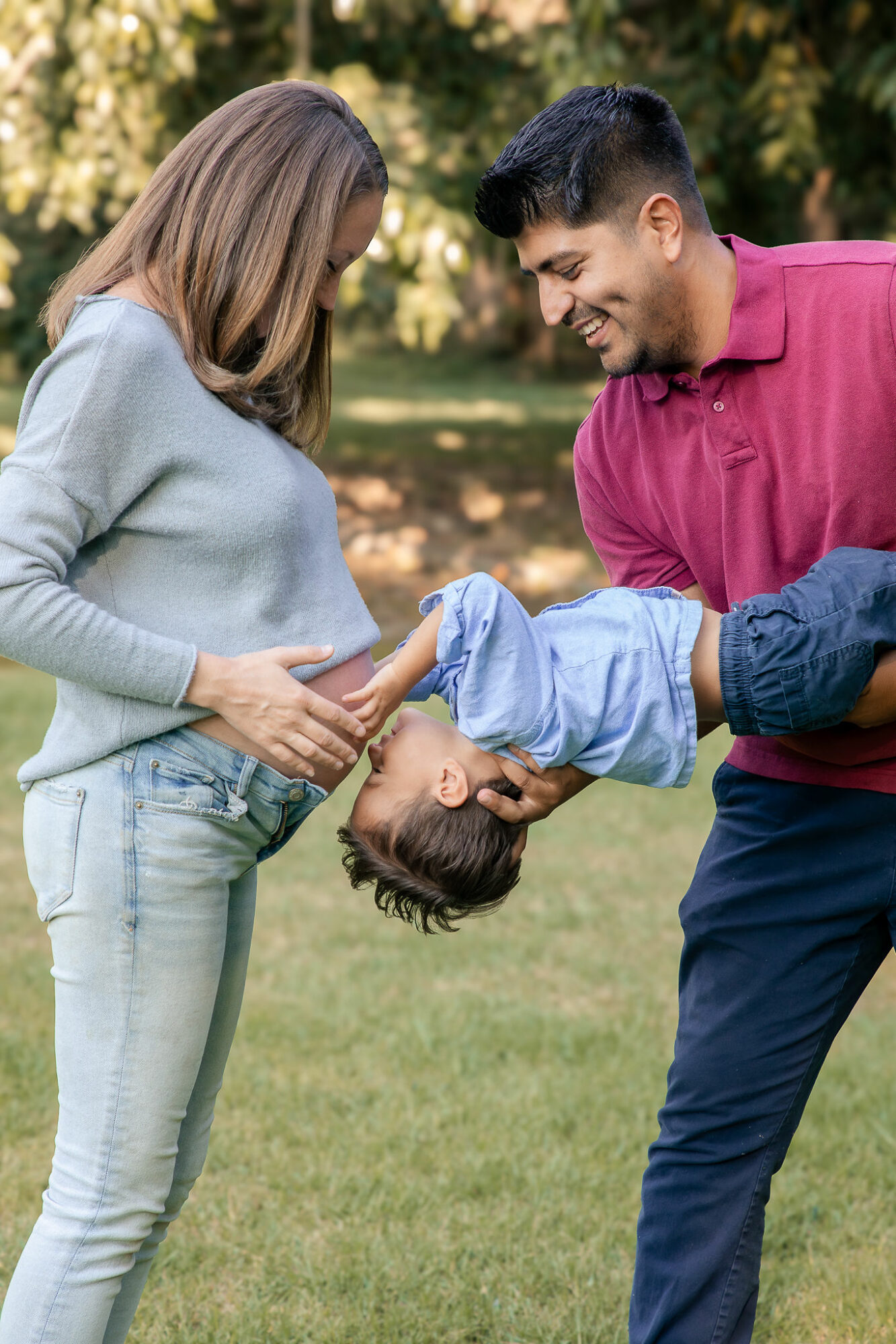 Two adults and a child outdoors, with the child upside down, smiling and holding hands with the adults.