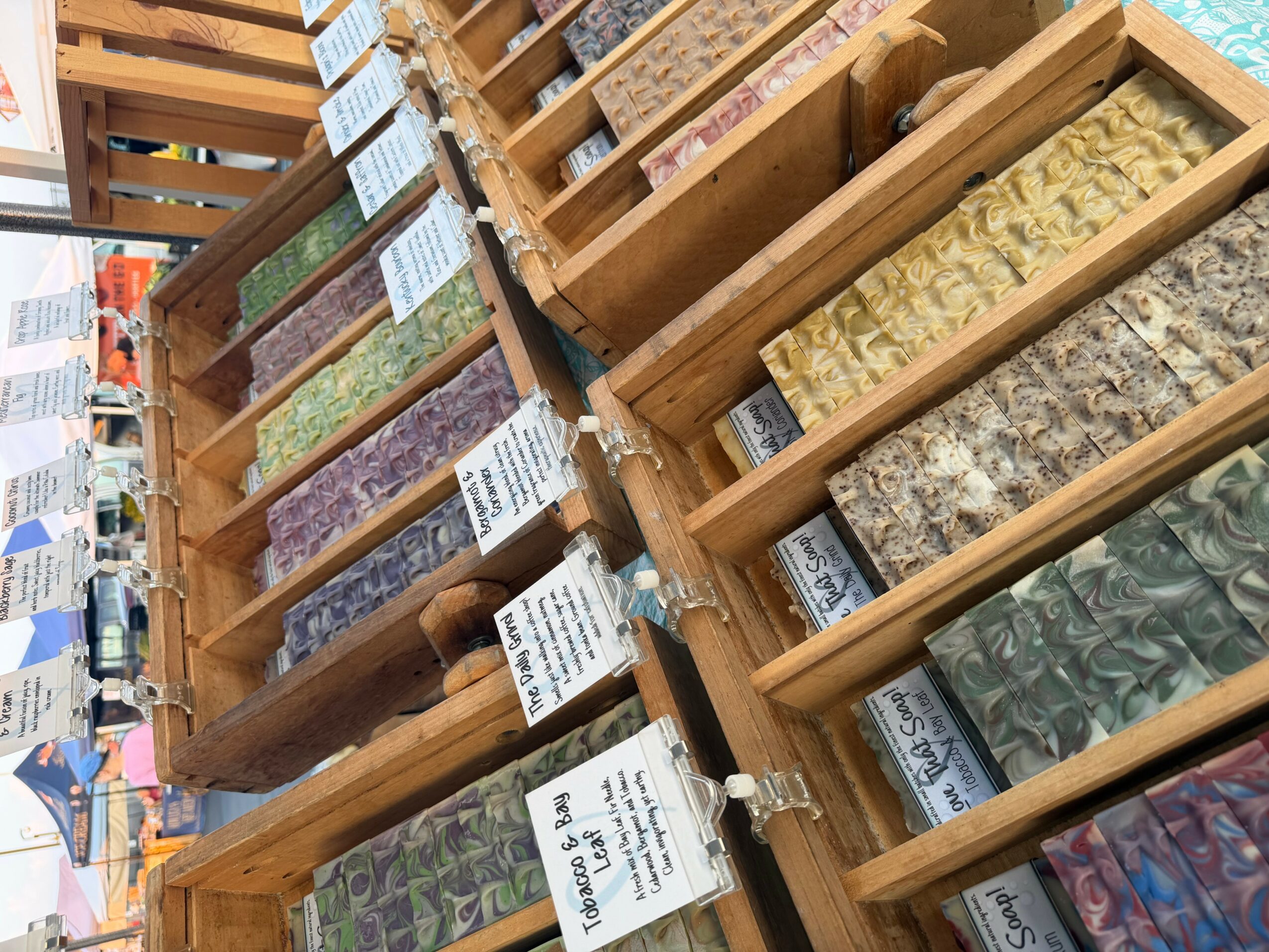 Display of various patterned tiles in wooden trays at a store, with price tags and labels visible.