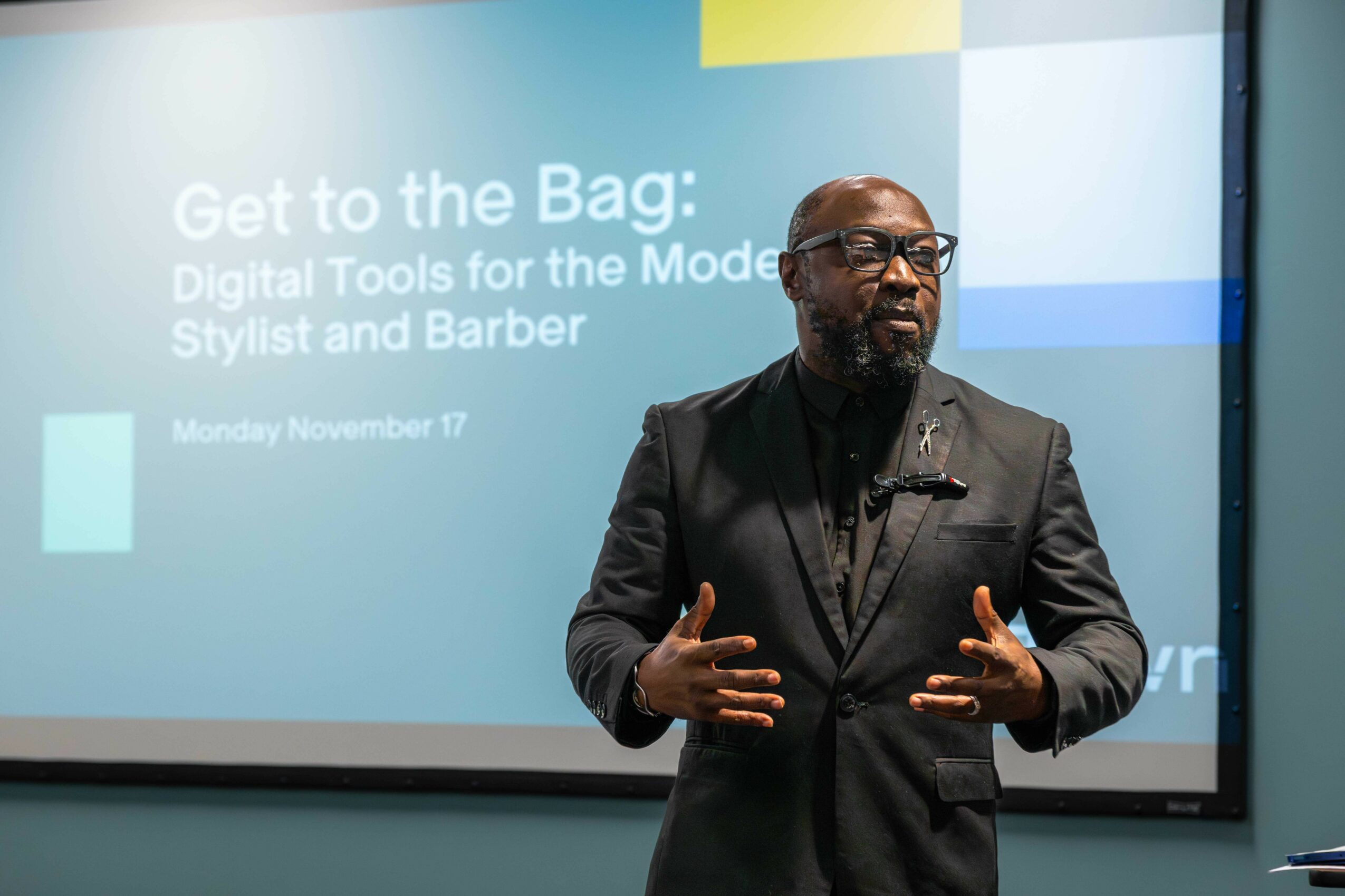 Man in dark suit speaking in front of a presentation screen with text about digital tools and styling, November 17.