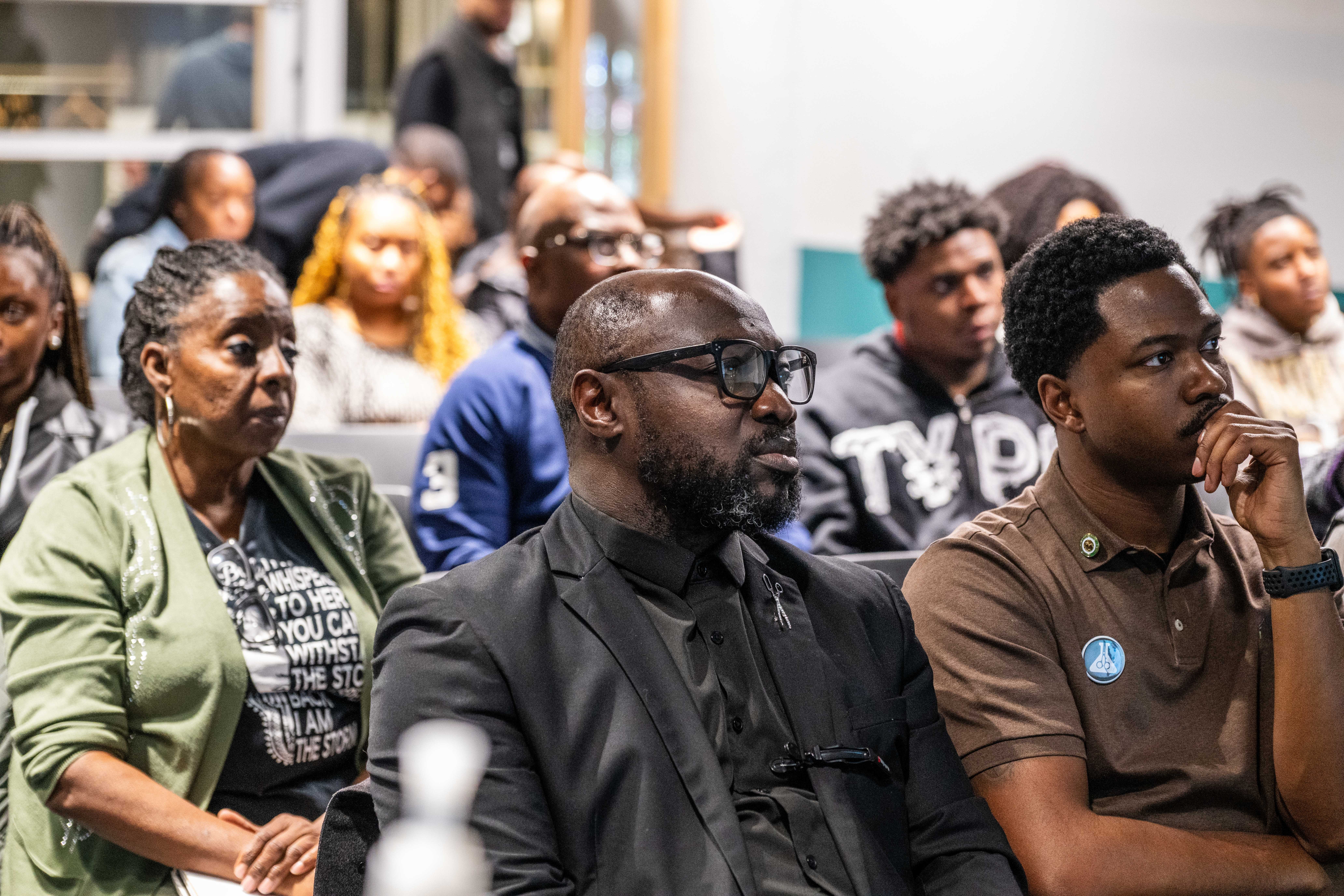 Group of diverse people seated indoors, attentively listening to a presentation or speaker.