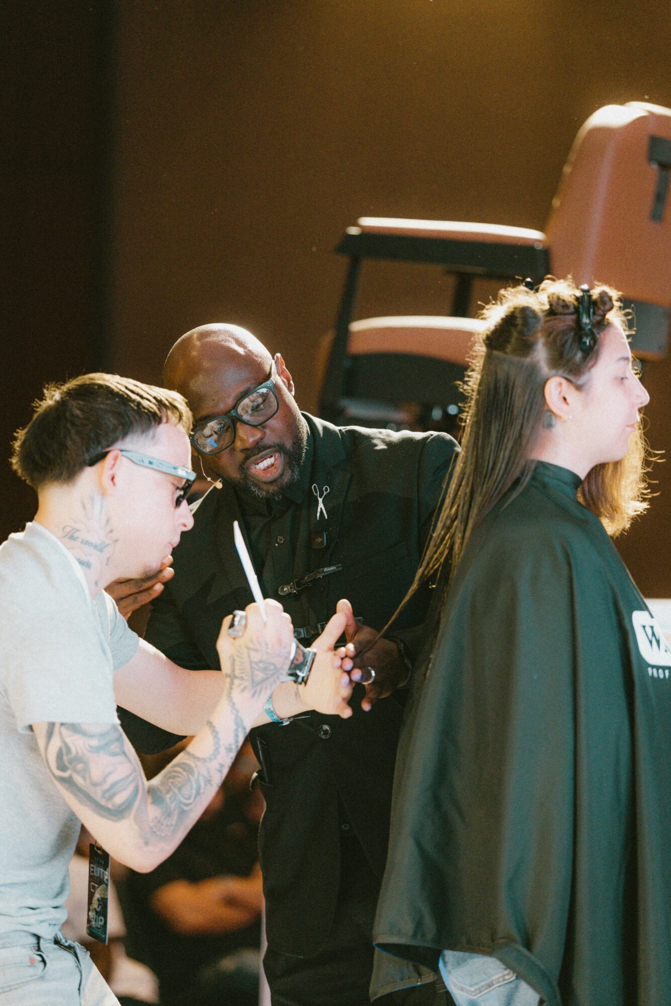 A person getting a haircut with two stylists, one holding scissors and the other smiling, in a salon setting.