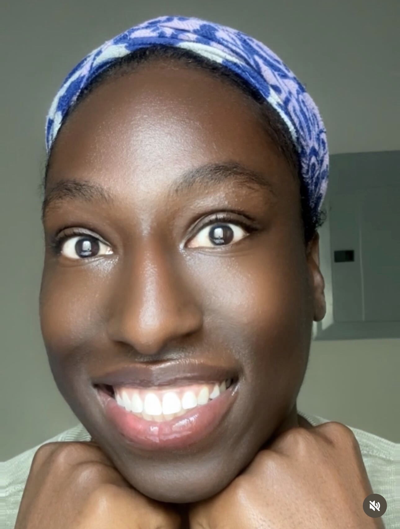Close-up of a smiling person with a blue patterned headscarf, bright eyes, and white teeth.