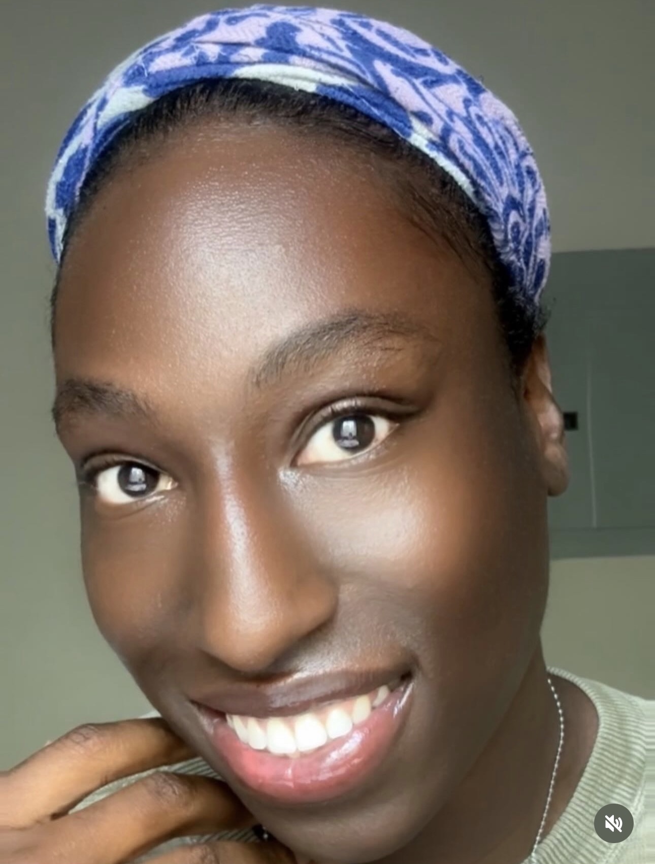 Close-up of a smiling woman wearing a blue patterned headscarf, with clear skin and bright eyes.