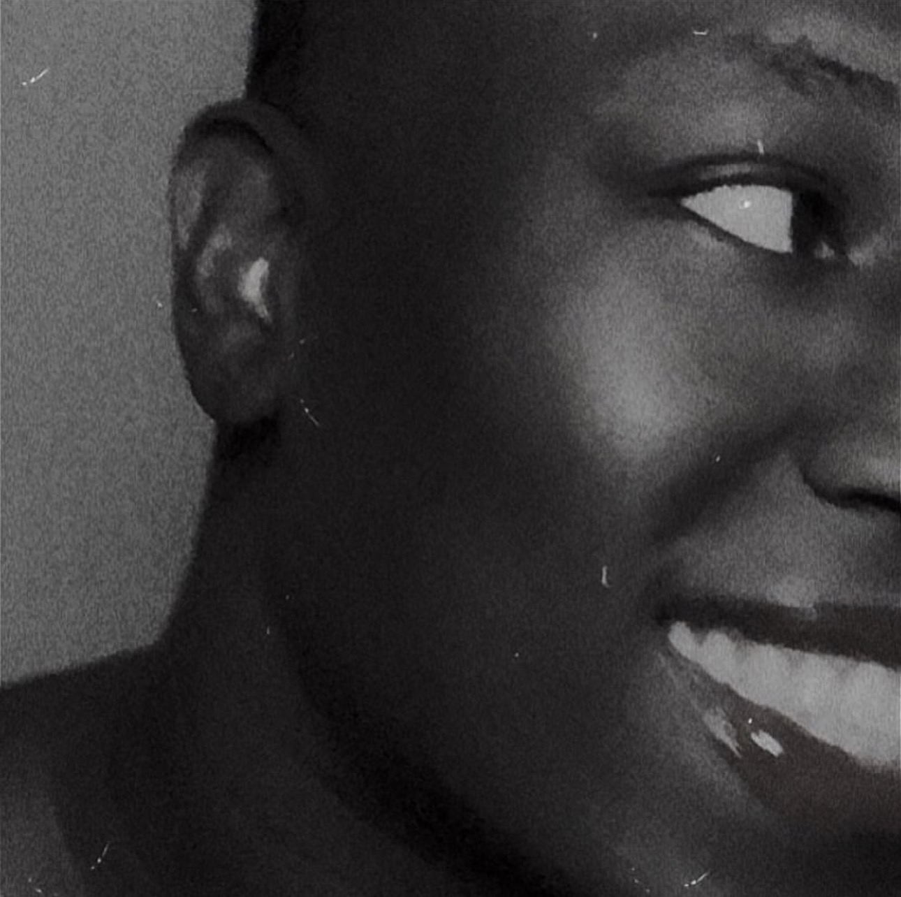 Close-up of a smiling person's face, showing eye, ear, and part of the mouth, in black and white.