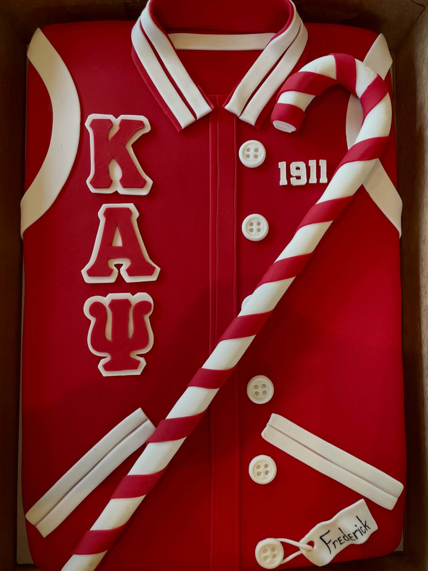 Red varsity jacket with white and red striped collar, white buttons, Greek letters, and a candy cane, with a tag reading 'Freshtown'.