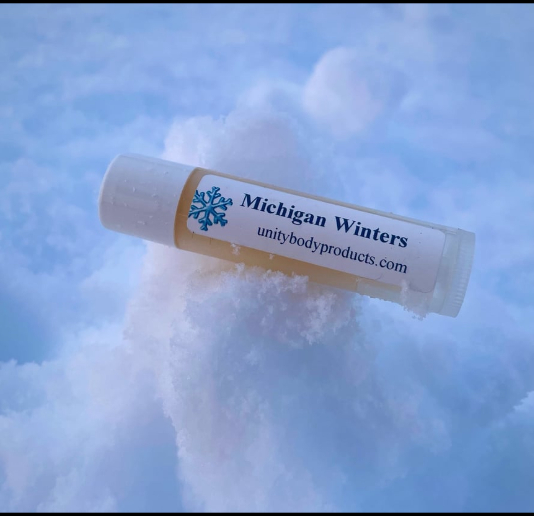 Lip balm tube labeled 'Michigan Winters' resting on snow, with a snow cloud in the background.