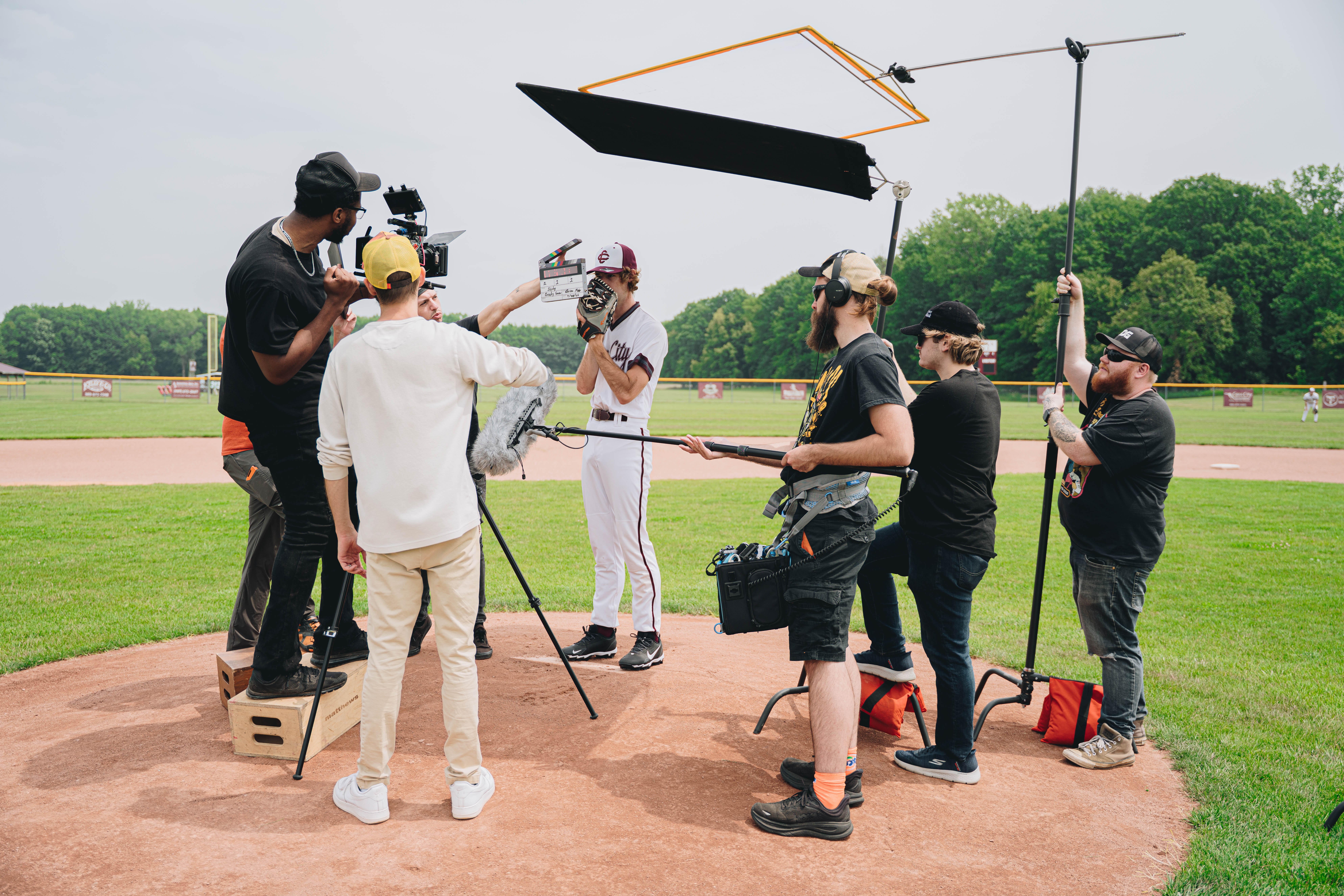 Group of people filming a baseball player on a field with equipment and a large reflector overhead.