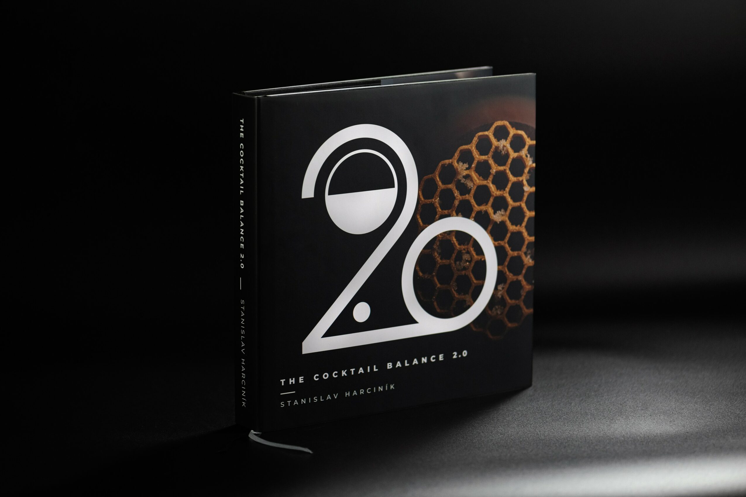 Black book with large white number 20 and honeycomb pattern on cover, titled 'The Cocktail Balance' by Stanley Macris, on dark surface.
