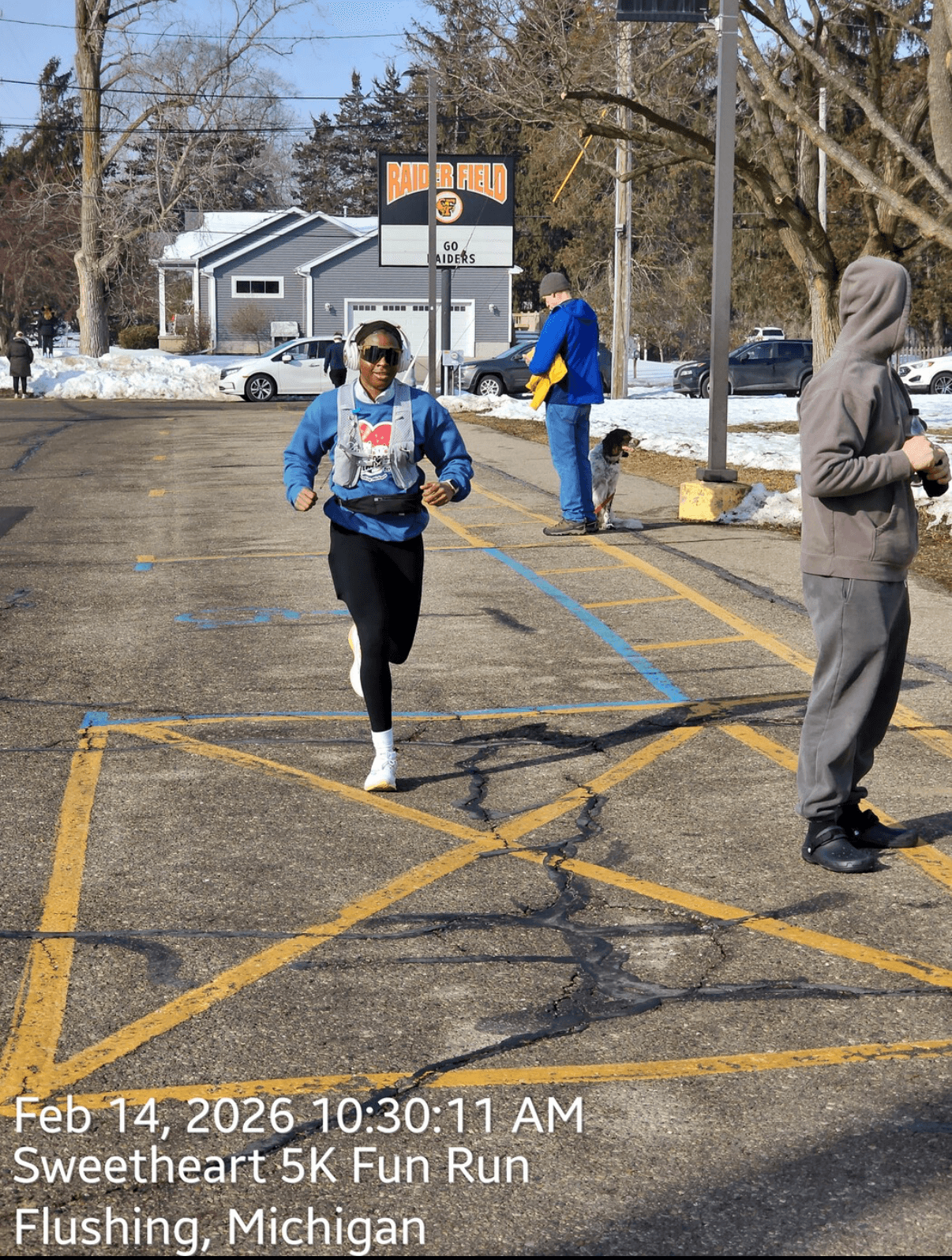 Person running in a parking lot during a race, with others nearby and snow on the ground, in Flushing, Michigan.