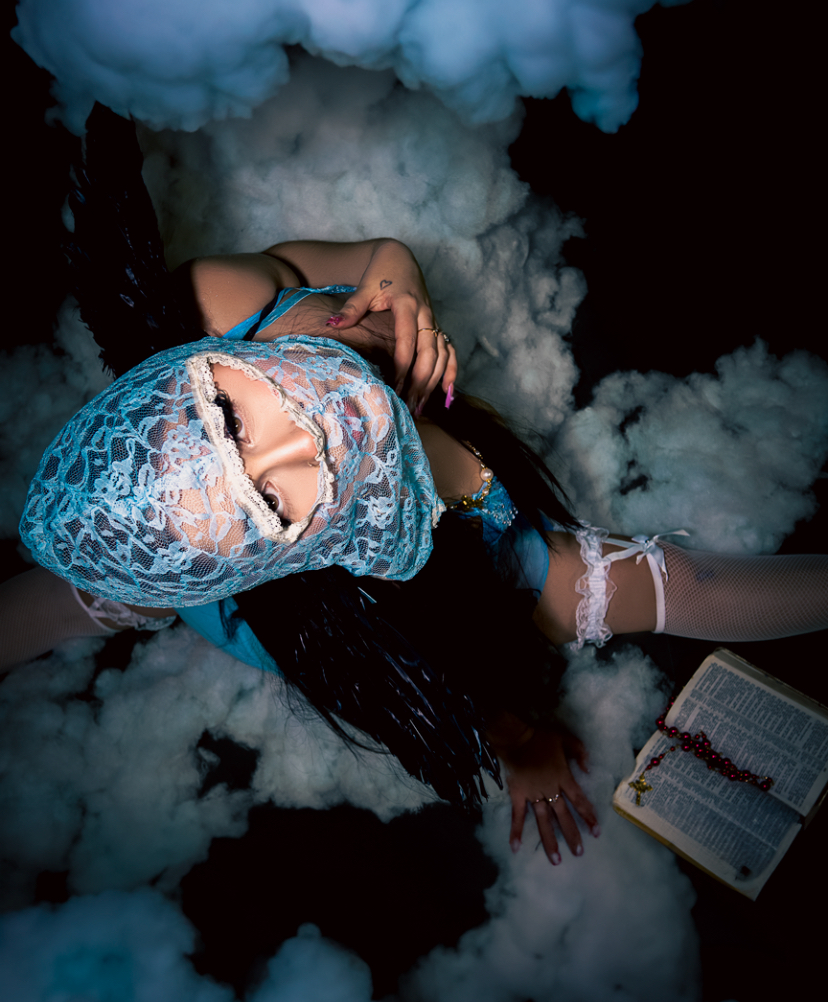 Person lying on clouds with a lace head covering, holding a book, surrounded by dark background and clouds.