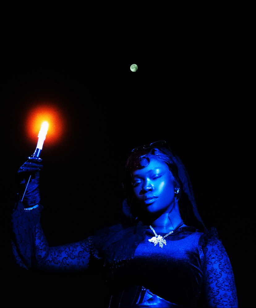 Woman holding a lit torch against a dark sky with the moon visible, illuminated in blue tones.