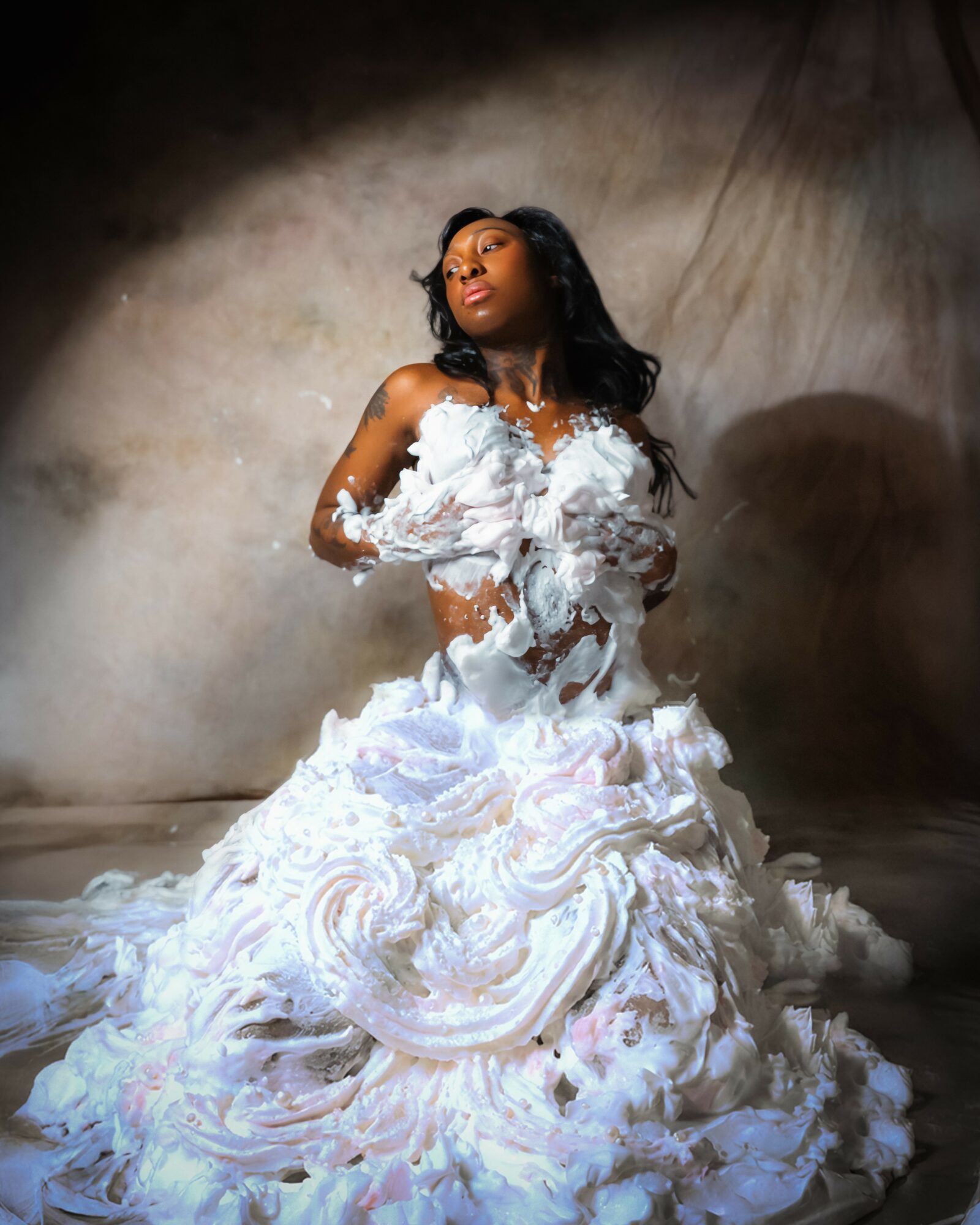 Woman in a white, ruffled dress with foam, standing against a neutral background, looking upward with a confident expression.