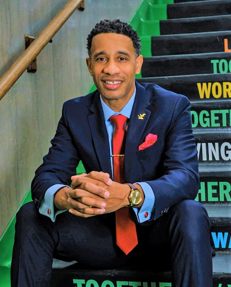 Man in a suit sitting on stairs, smiling, with colorful words on the steps behind him.