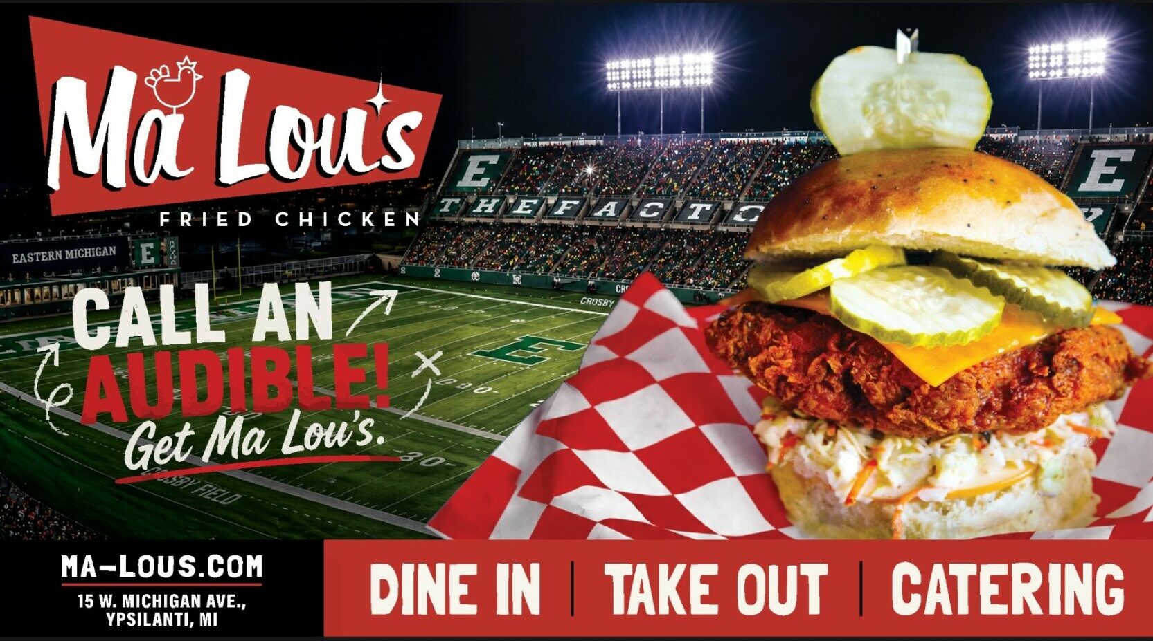 Fried chicken sandwich with lettuce, pickles, and onion on a bun, with a pumpkin on top, in a stadium setting.