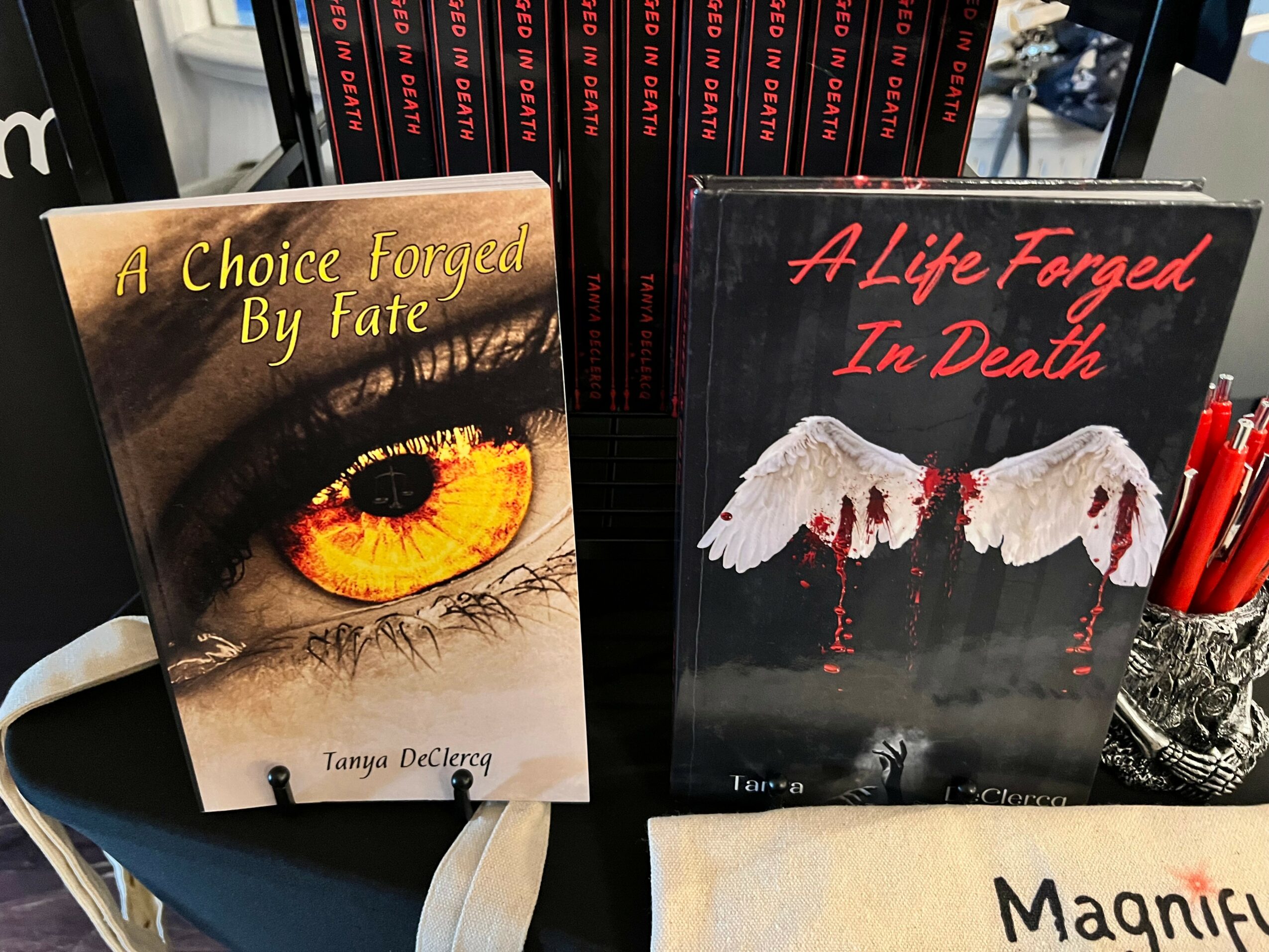 Two books displayed upright, one with a close-up eye and the other with wings and blood, on a shelf.