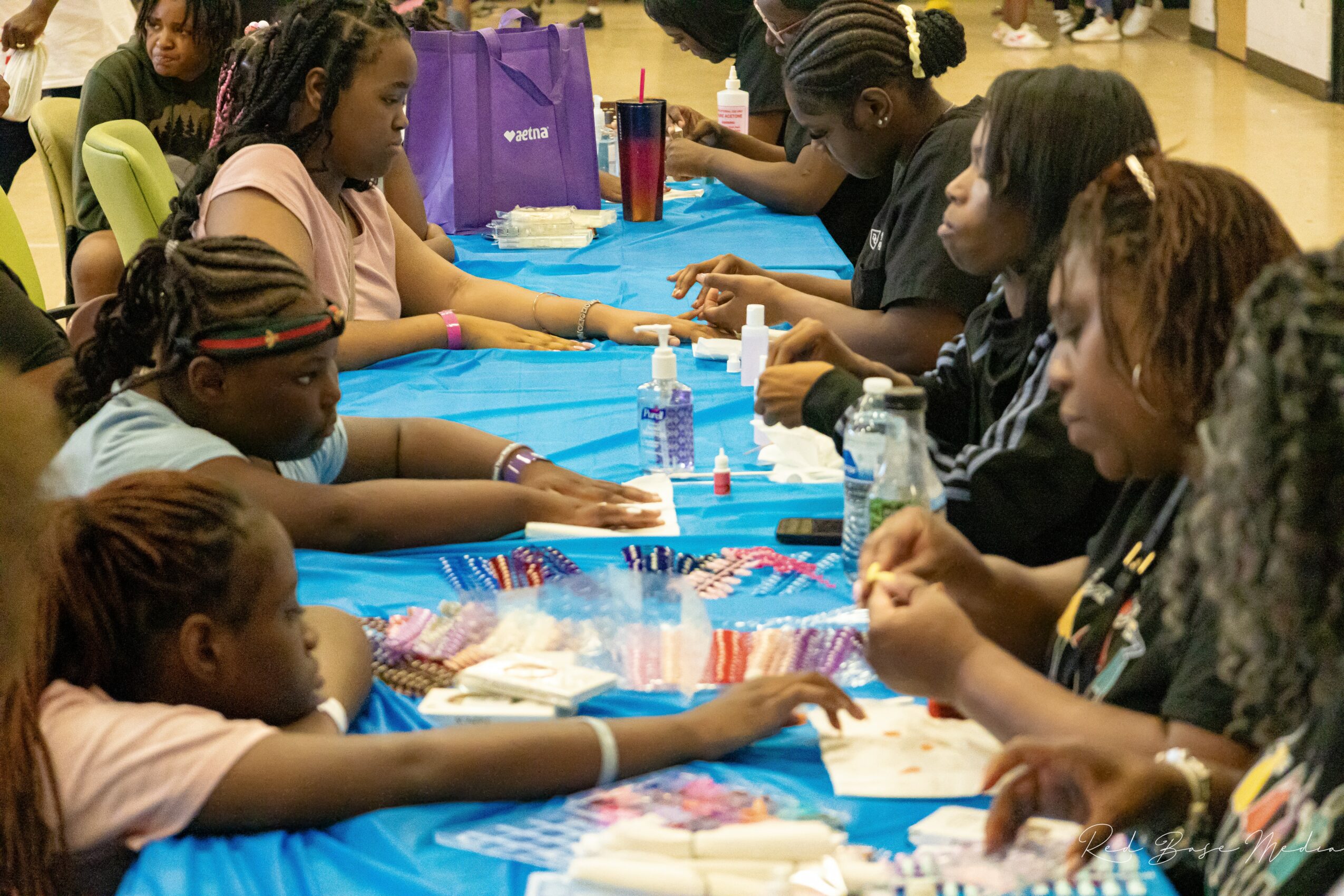 Children and adults sit at a table with arts and crafts supplies, engaging in a group activity indoors.