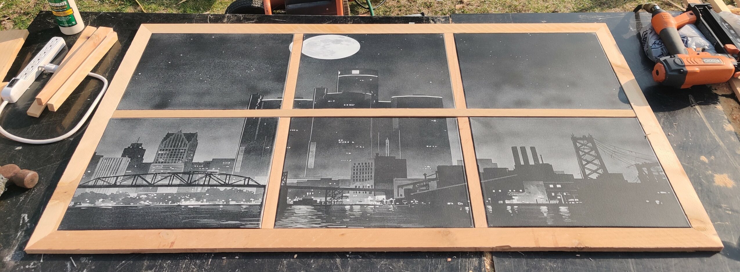 Six black and white cityscape photographs arranged in a grid on a wooden frame, with tools and equipment around them.